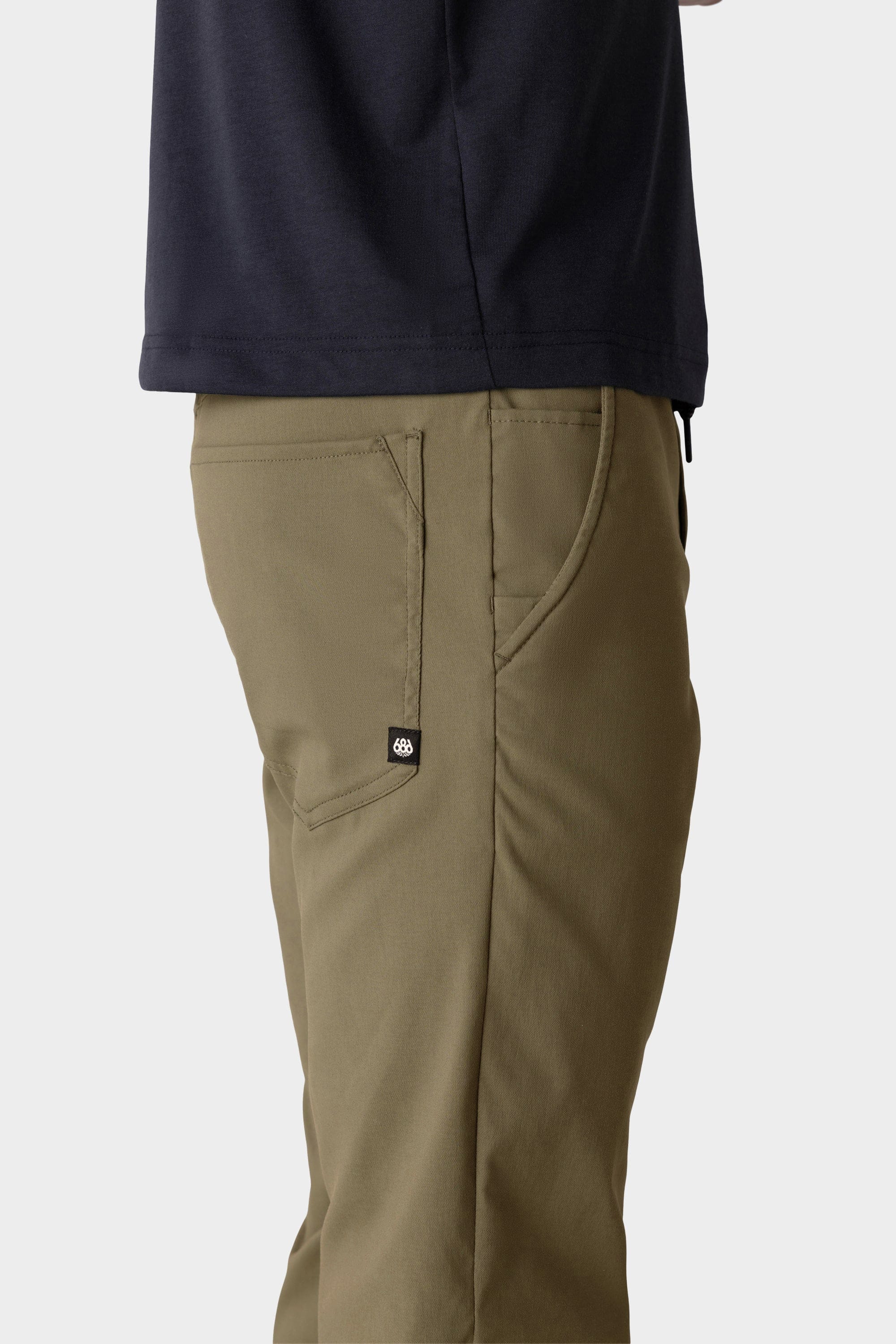 A person in 686 Men's Everywhere® Merino-Lined Pant - Slim Fit stands side-on, highlighting the pants’ pocket and black logo tag—ideal for warmth in cold weather.