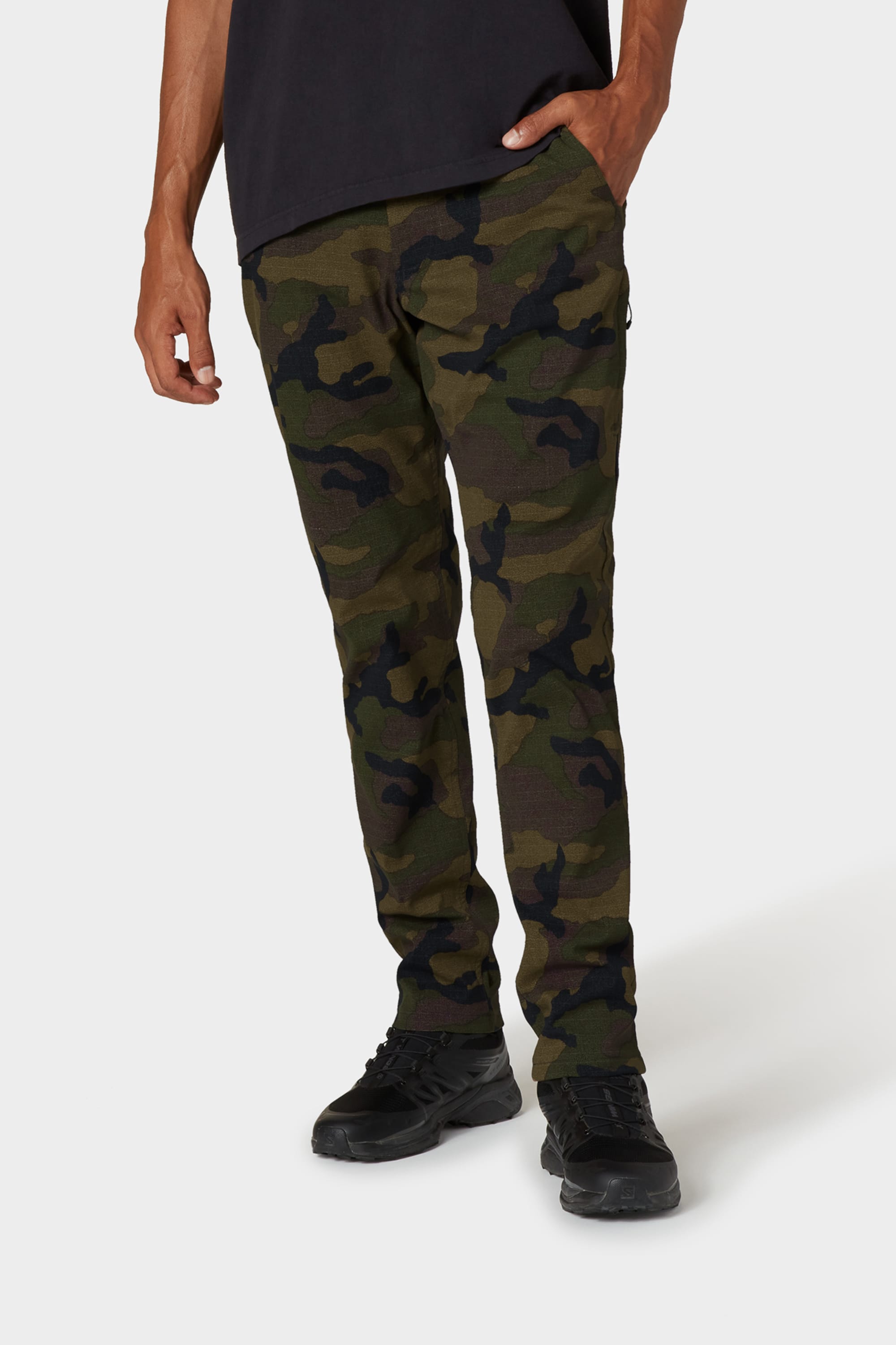 Dressed for colder weather, a person stands against a plain background wearing 686 Men's Everywhere® Merino-Lined Pant - Slim Fit, a black shirt, and black shoes, with one hand in their pocket.