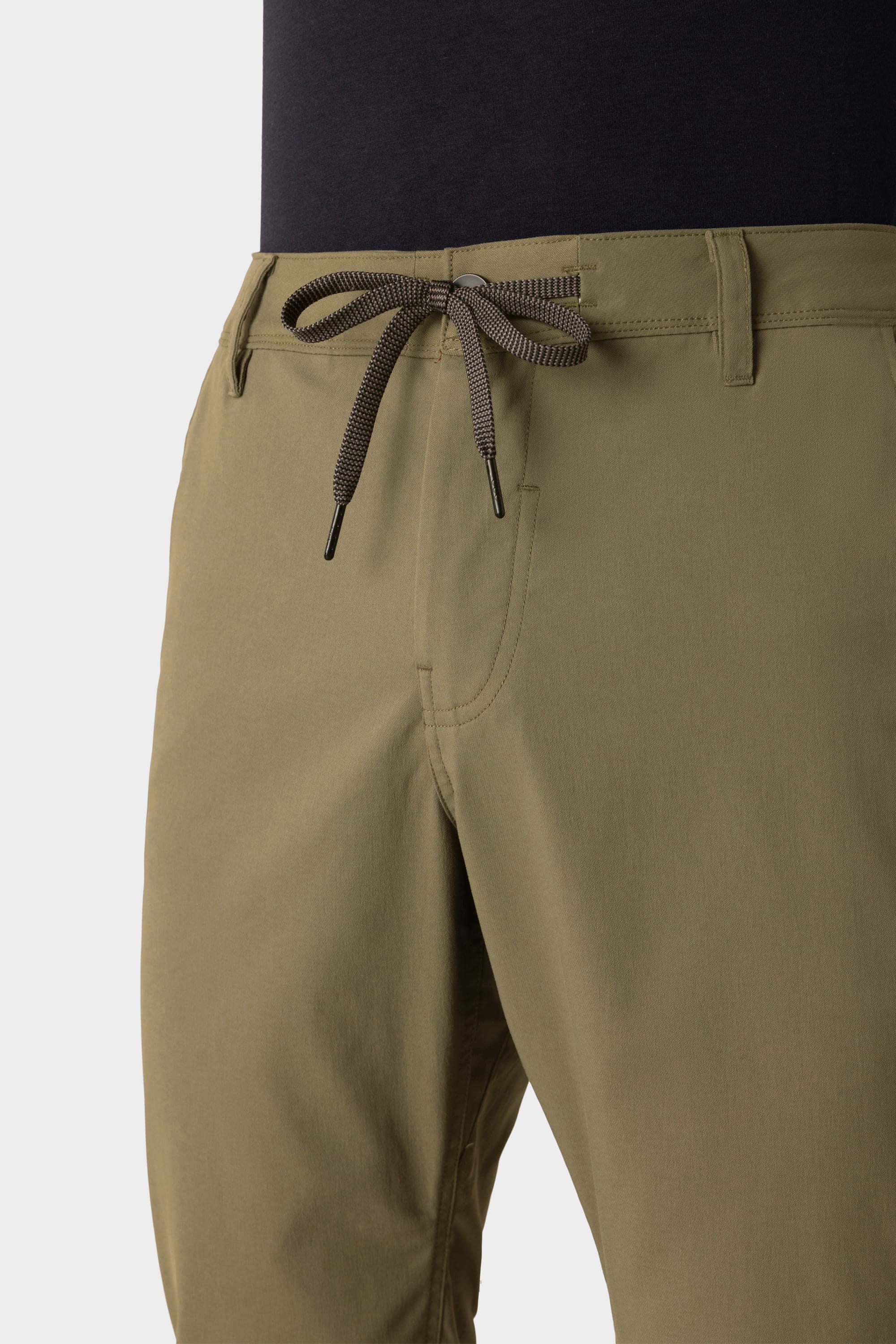 A close-up of a person wearing the 686 Men's Everywhere® Pant - Relaxed Fit in olive green, featuring a black drawstring waist, side pockets, and belt loops. Paired with a dark top, these breathable 686 pants offer comfort and style.
