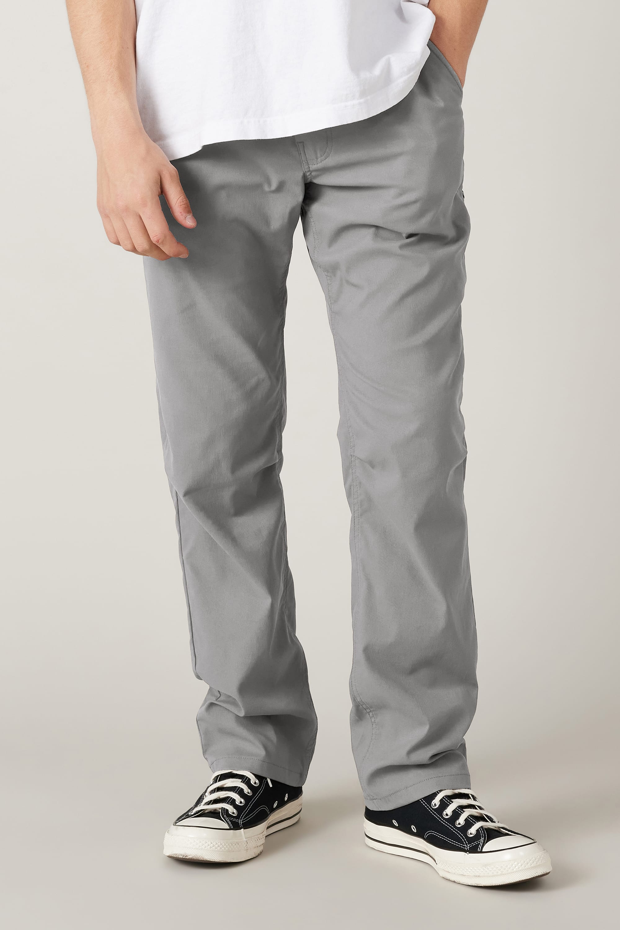 A person wearing the 686 Men's Everywhere® Pant - Relaxed Fit in light gray, a white T-shirt, and black low-top sneakers with white soles stands with one hand in a pocket; only their lower half is shown against a plain background.