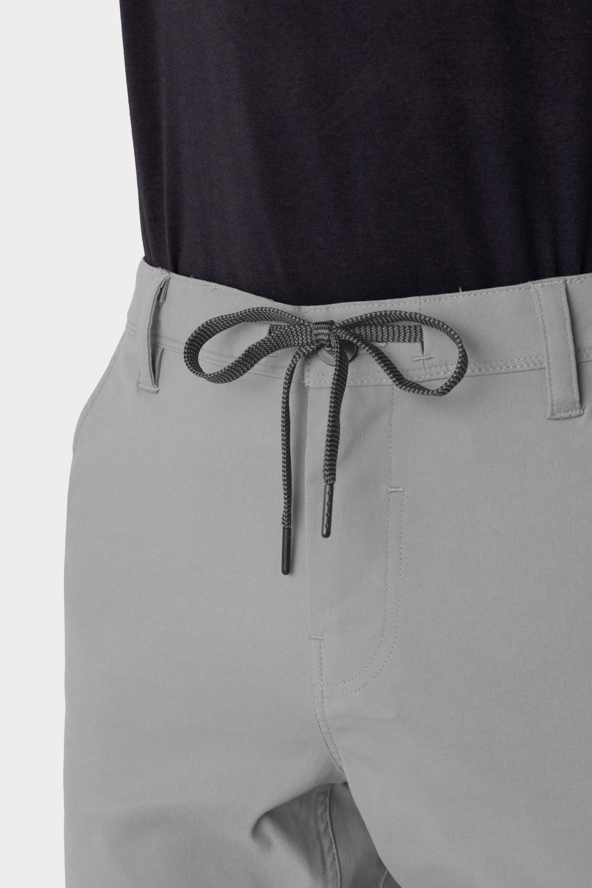 Close-up of the 686 Men's Everywhere® Pant - Relaxed Fit in light gray, featuring stain-resistant fabric and a black drawstring waistband, paired with a dark shirt. Only the waist and upper thighs are shown.