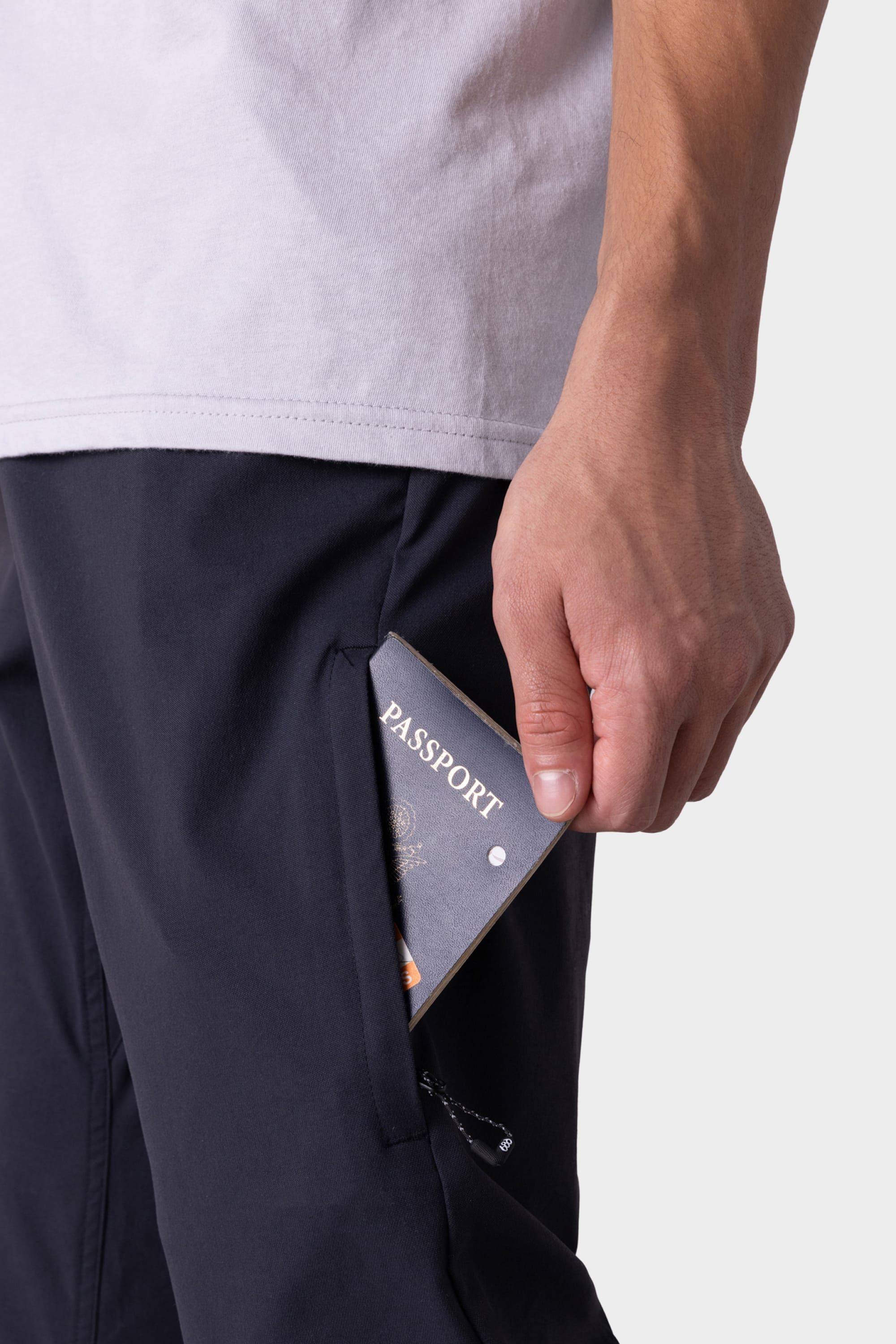A person in a white shirt and the 686 Men's Everywhere® Pant - Relaxed Fit by 686 puts a passport into a zippered side pocket on their pants.