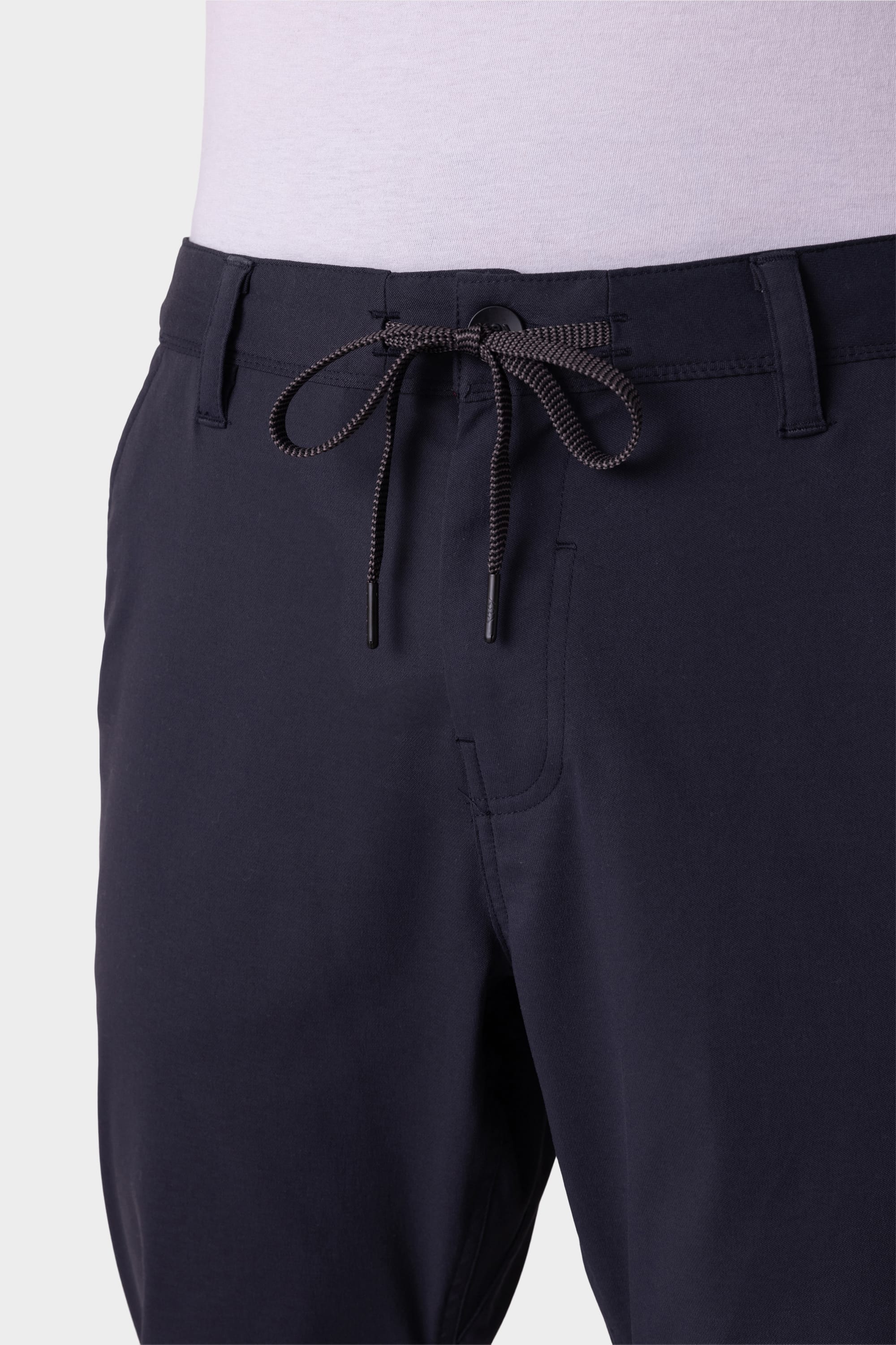 A close-up shows a person wearing 686 Men's Everywhere® Pant - Relaxed Fit in a dark color, featuring a visible drawstring at the waistband and belt loops, paired with a light-colored shirt.