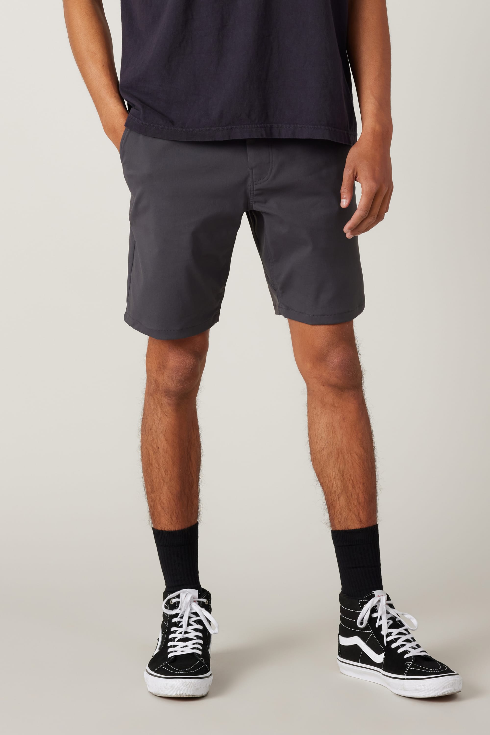 A person wearing a black T-shirt, 686 Everywhere® Hybrid Short by 686, black crew socks, and black high-top sneakers stands with one hand in their pocket against a plain background.