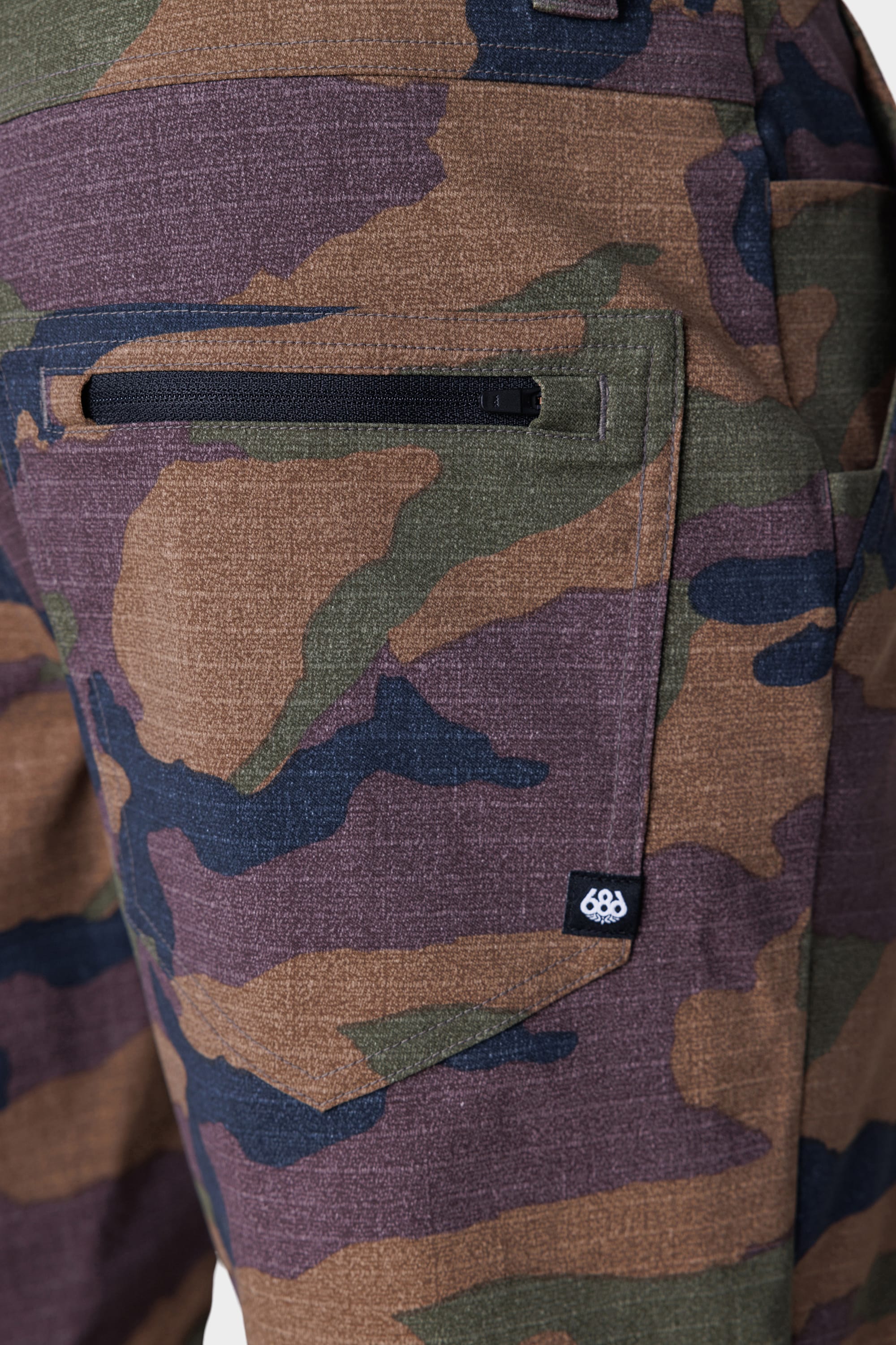 Close-up of the side pocket on the 686 Everywhere® Hybrid Short by 686, showing a camouflage pattern in green, brown, and black with a small black and white logo tag near the stain-resistant pocket.