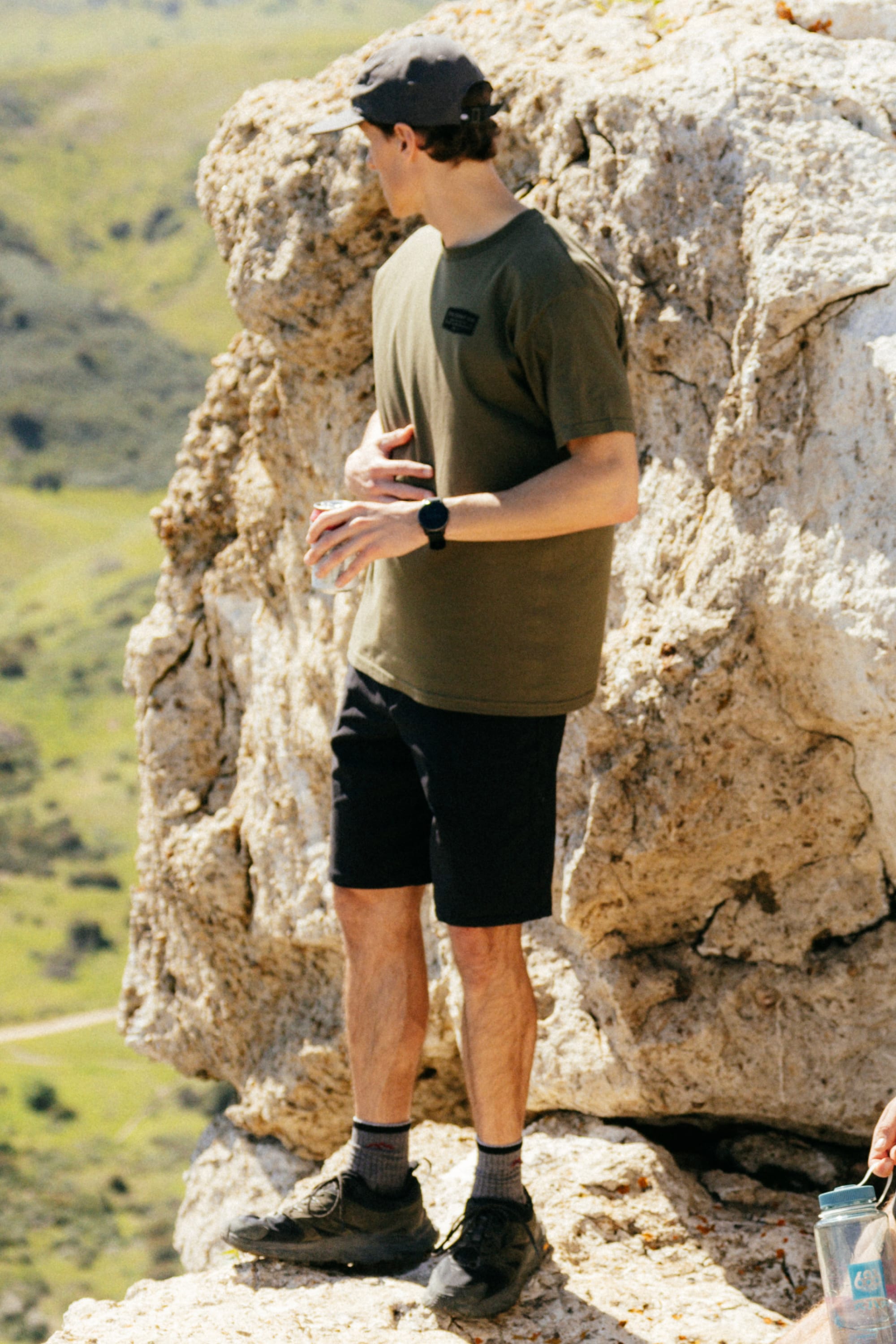 A man stands on a rock, wearing 686 Everywhere® Hybrid Short - Relaxed Fit by 686, breathable shorts designed for comfort and style on any adventure.