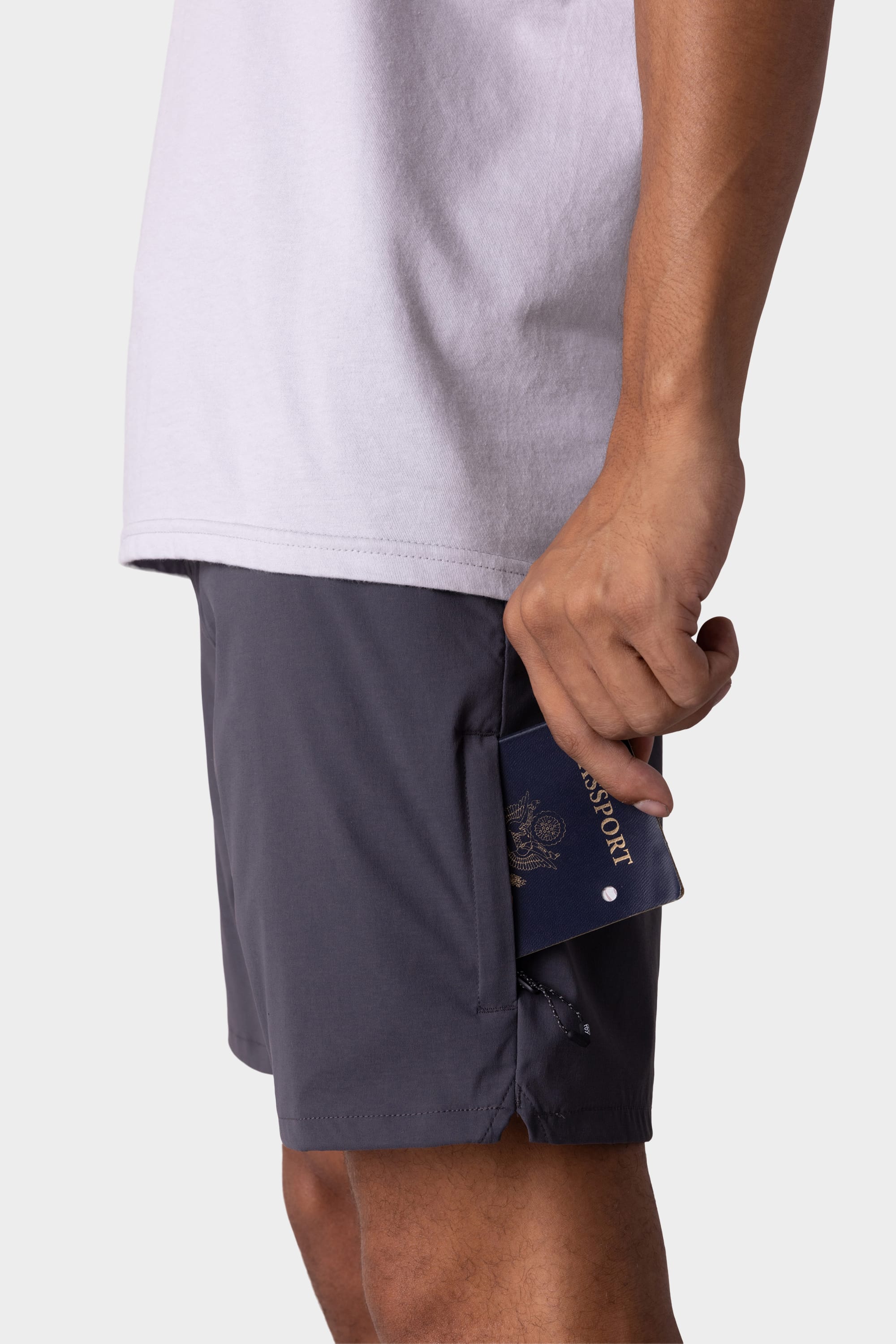 Wearing 686 Men's Everywhere® Featherlight Chino Short, a person slips a navy blue passport into the side pocket of their shorts.