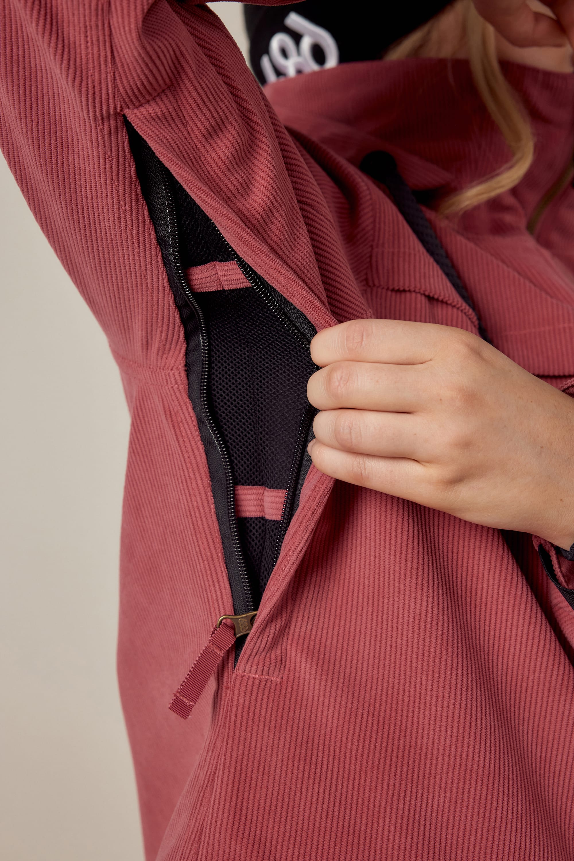 A person wearing the 686 Womens Spirit Insulated Jacket in pink unzips a side vent, revealing black mesh lining and pink straps inside the jacket.
