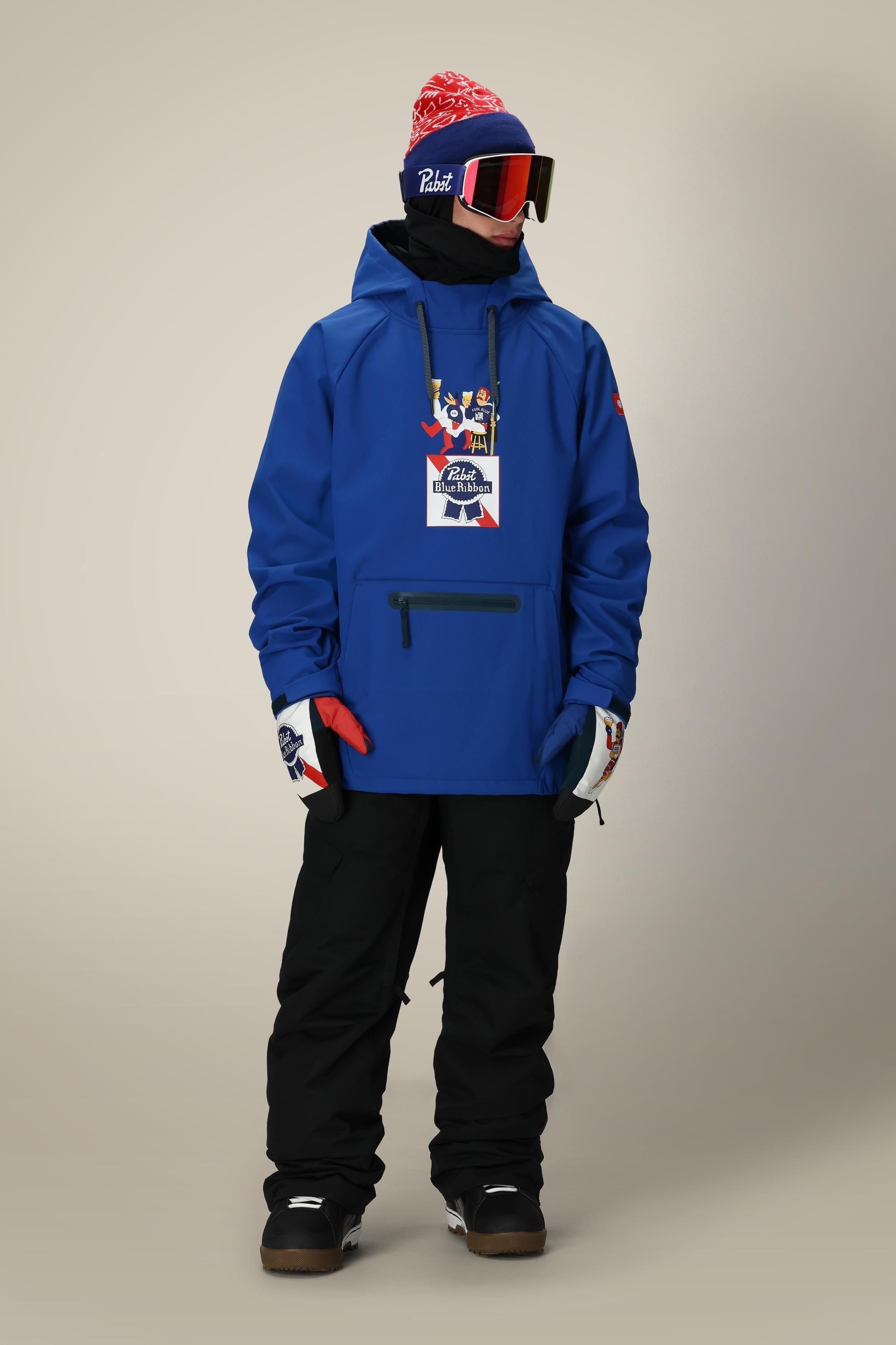 A person wearing the 686 Mens Waterproof Hoody, black snow pants, gloves, brown boots, a red and white beanie, neck warmer, and ski goggles stands against a neutral background.