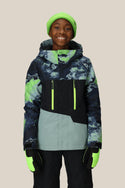 A smiling child wears the 686 Boys' Geo™ Insulated Jacket with blue and green camouflage patterns, paired with a neon green beanie and gloves, plus black snow pants—ready for comfort against a plain light background.