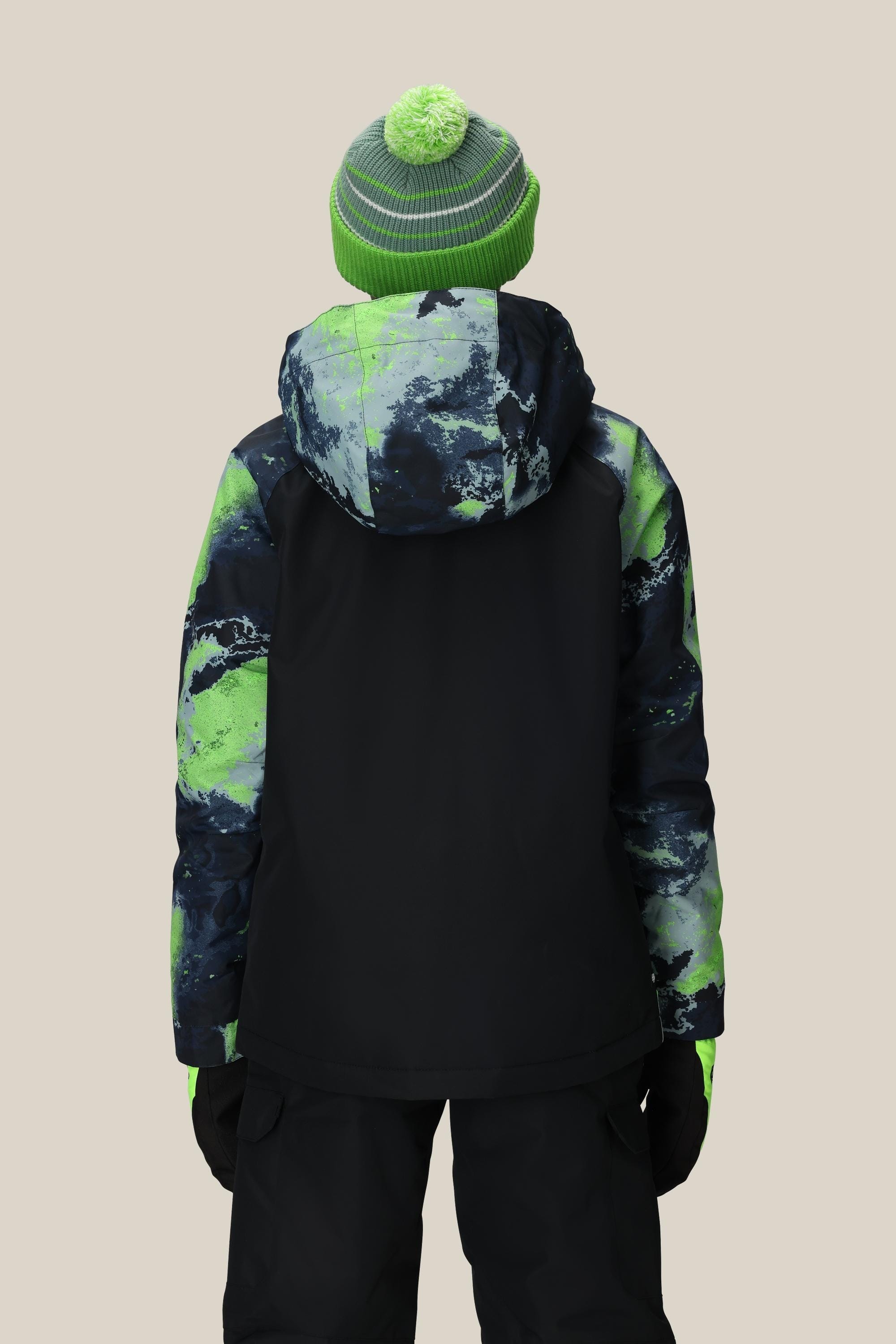 A person wears the 686 Boys' Geo™ Insulated Jacket in green and black, paired with black gloves, black pants, and a green knit pom-pom beanie, standing with their back to the camera against a beige background.