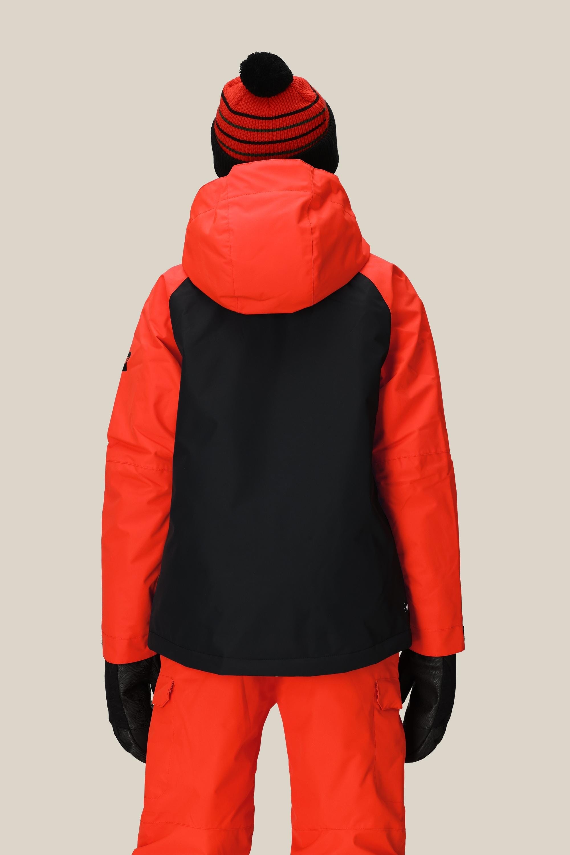 A child wearing a 686 Boys' Hydra™ Insulated Jacket, matching red snow pants, black gloves, and a red and black pom-pom knit hat, seen from the back against a plain light background.