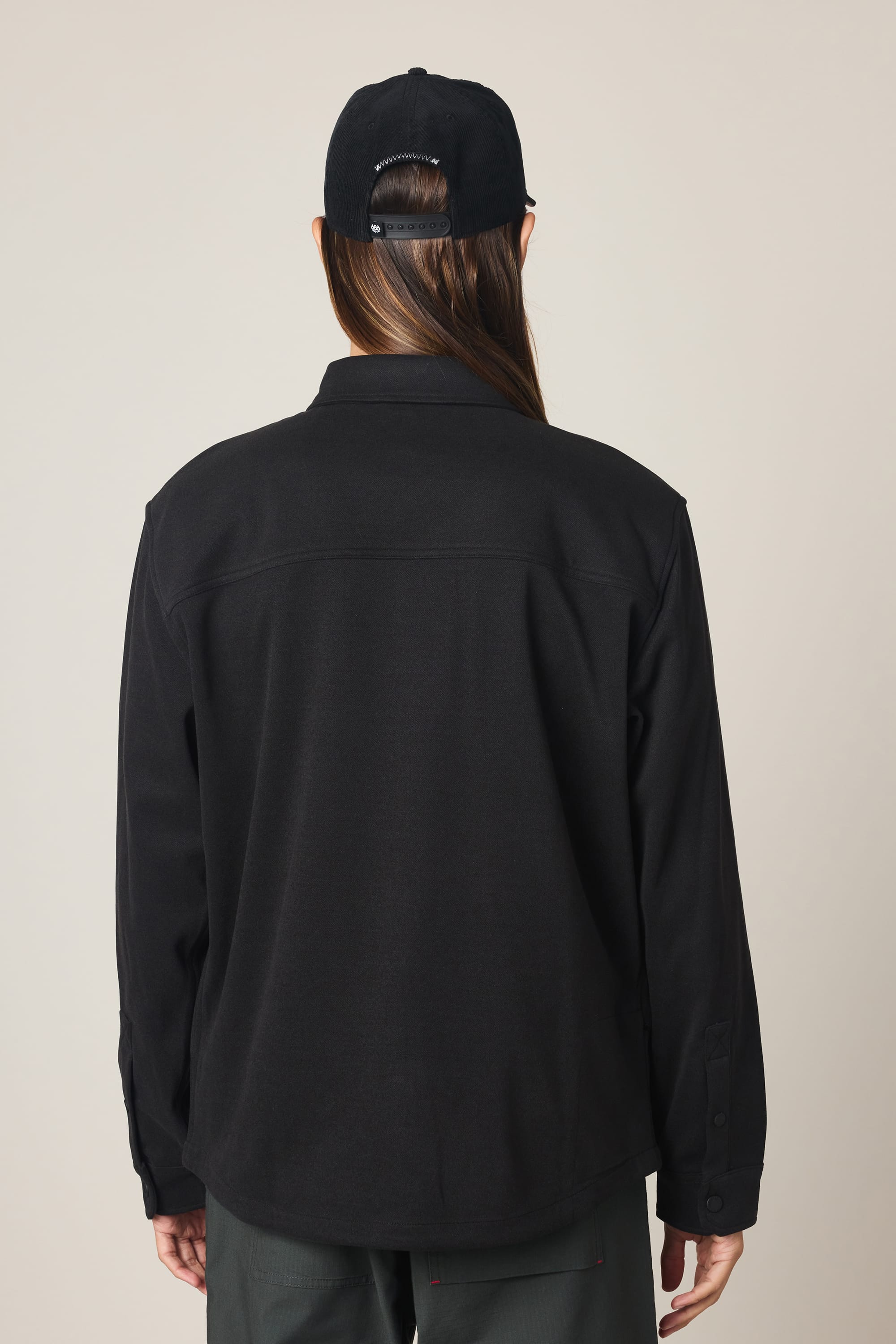 A person with long brown hair, wearing a black 686 Men's Whisper Knit Flannel and dark pants, is shown from the back against a plain light background.