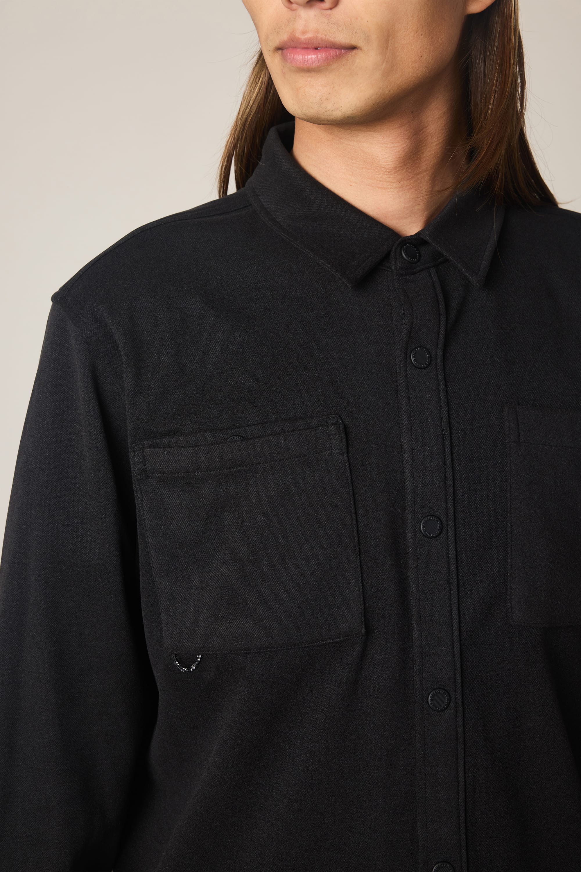 A person with long brown hair wears a black 686 Men's Whisper Knit Flannel shirt, photographed from the shoulders up against a plain background.