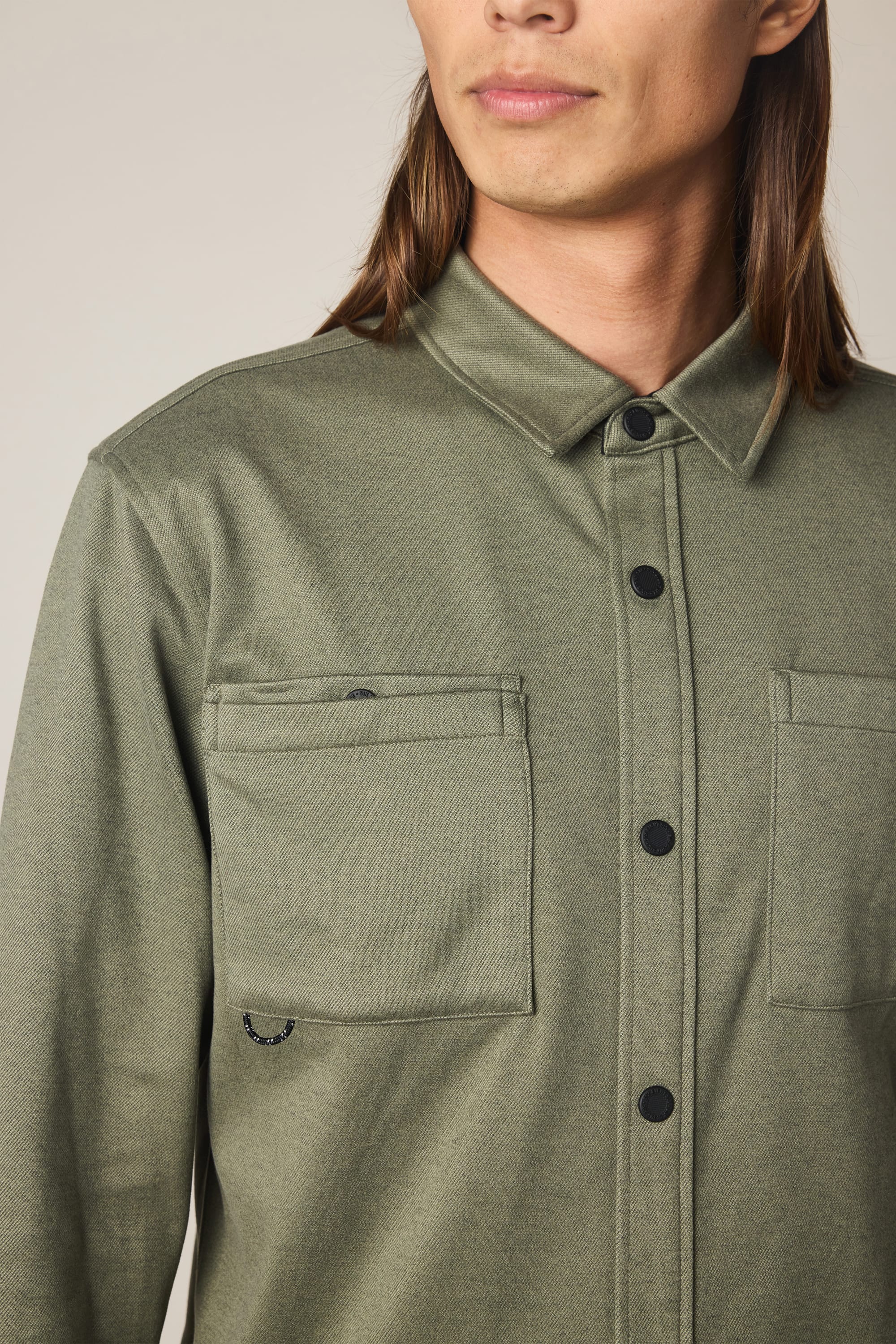 A person with long brown hair wears the 686 Men's Whisper Knit Flannel in olive green. The image, cropped at the shoulders, shows only the lower half of their face and upper torso.