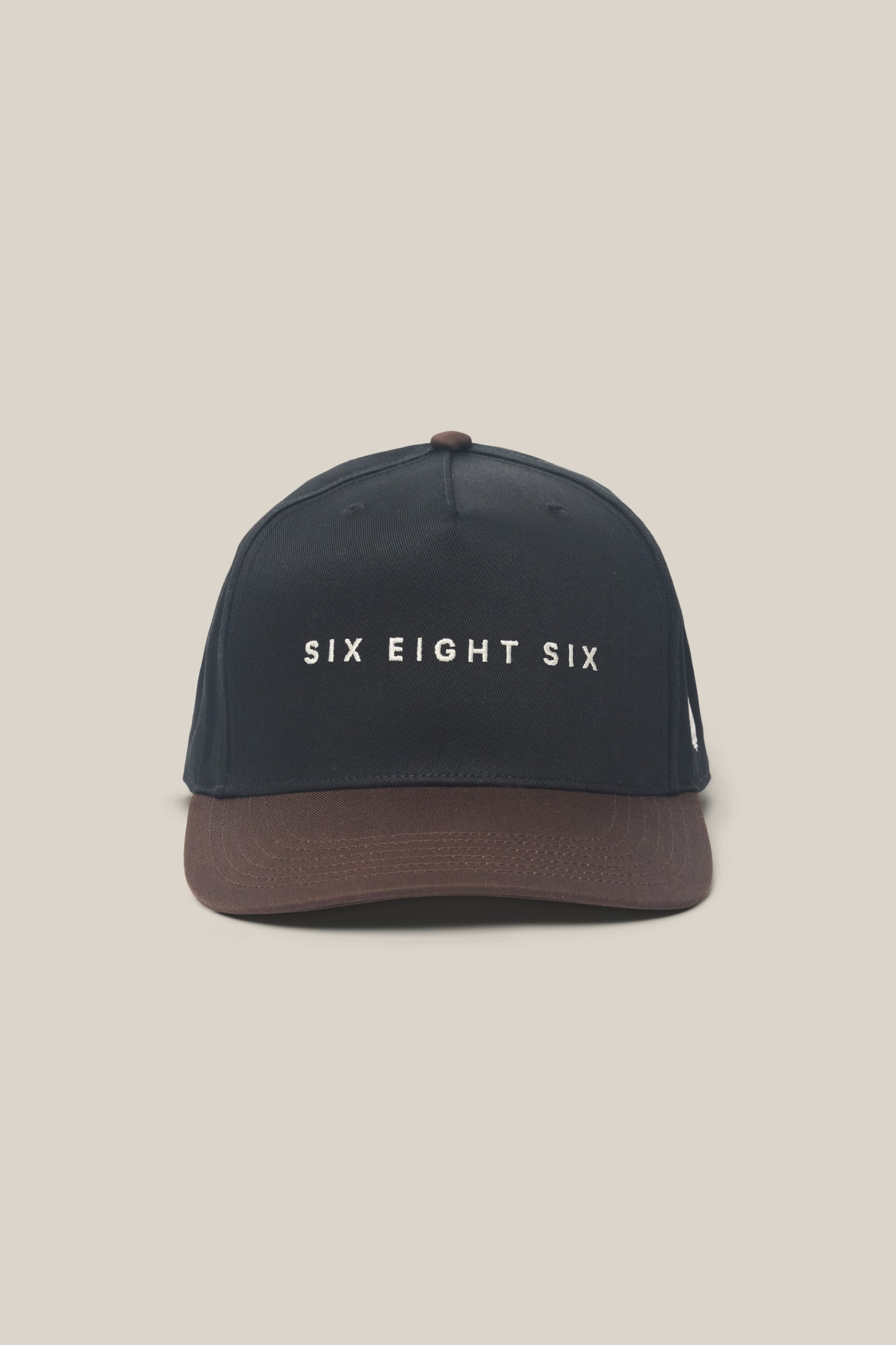 The 686 High-Pro Ses Two Tone Structured 5 Panel Hat by 686 is a black men‚Äôs hat with a brown brim, made from 100% cotton and featuring "SIX EIGHT SIX" in white letters on the front, shown against a plain beige background.