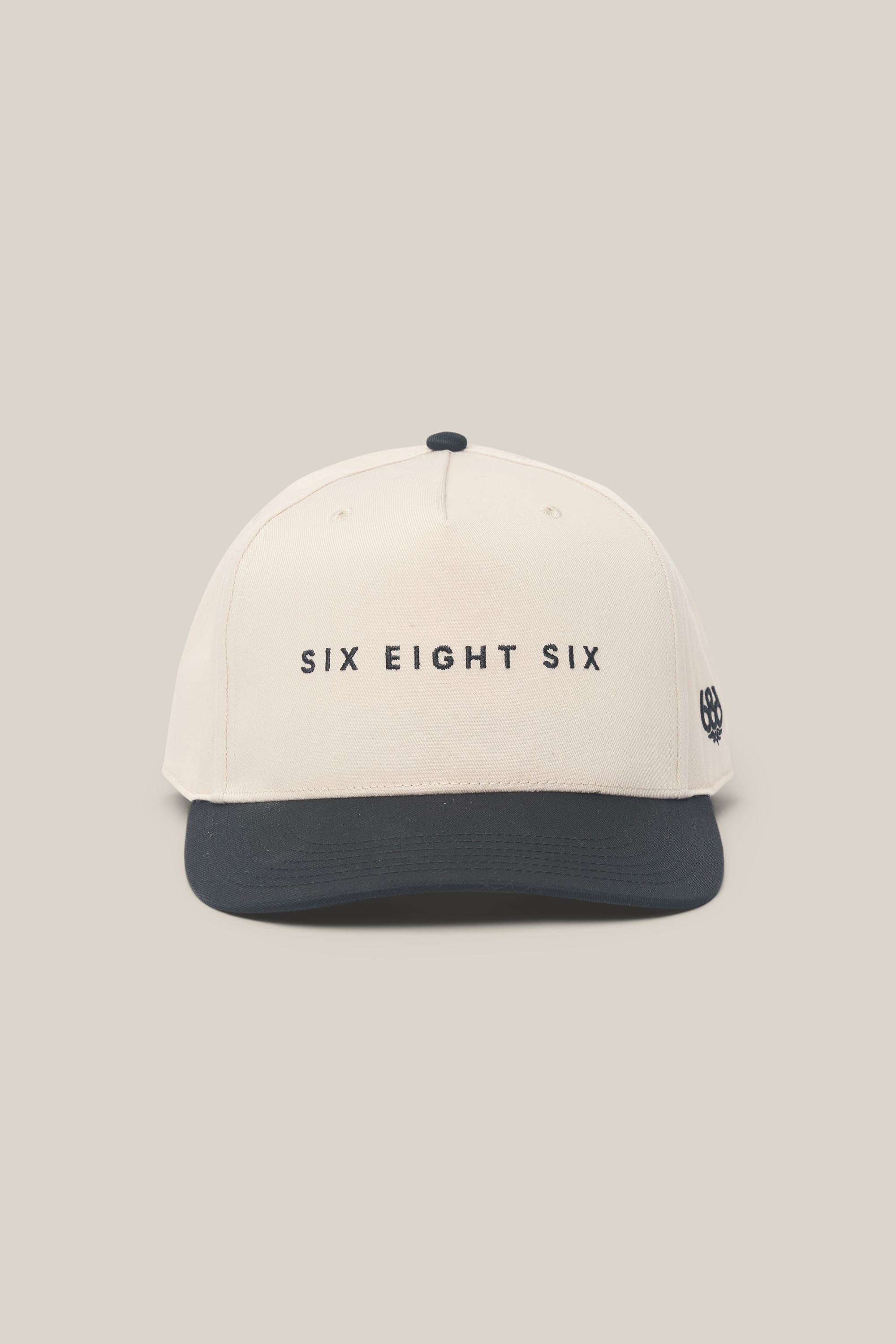 Introducing the 686 High-Pro Ses Two Tone Structured 5 Panel Hat by 686—a beige cotton men’s hat with a black brim and “SIX EIGHT SIX” embroidered in black on the front, blending classic style and everyday comfort.