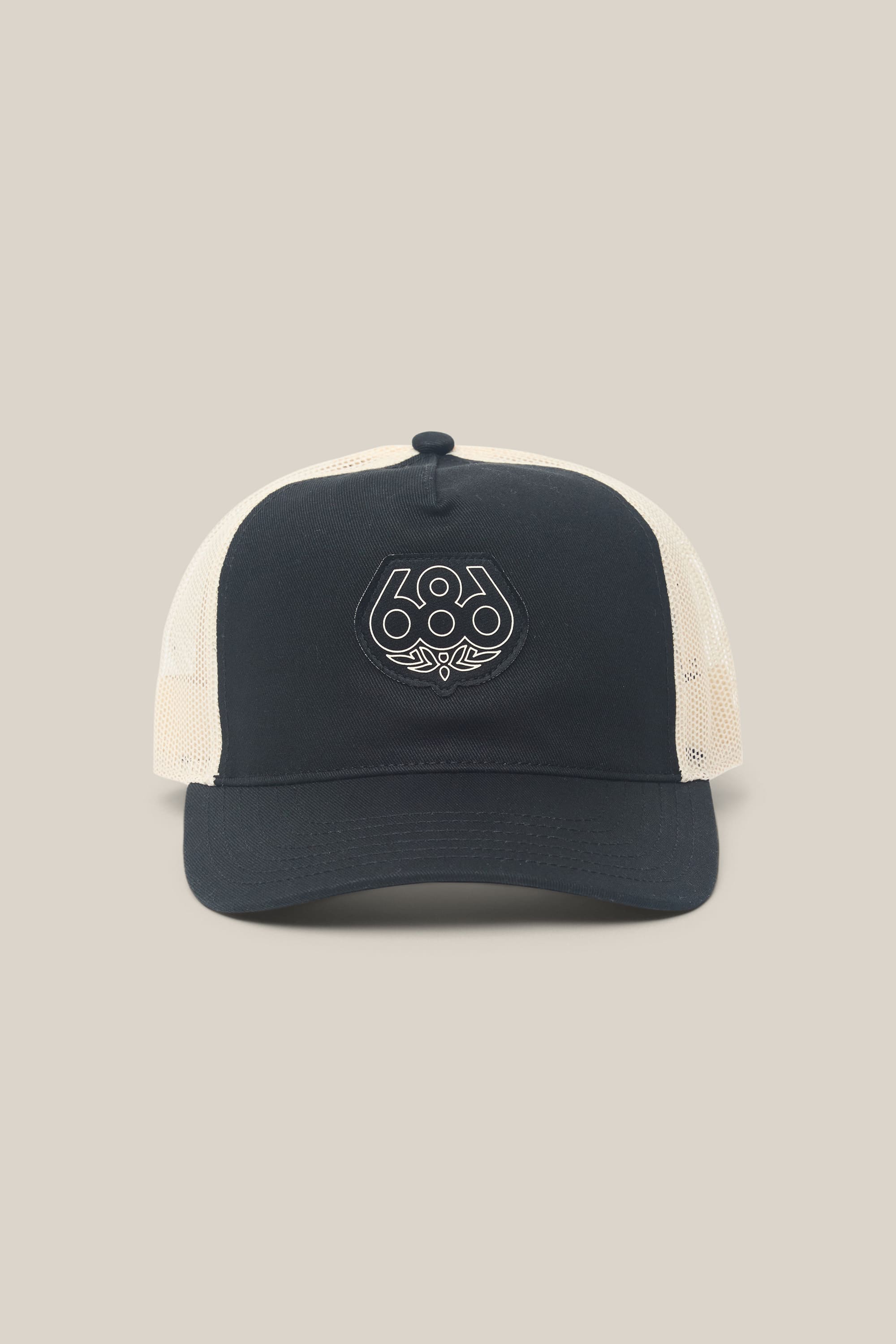 The 686 Mid-Pro Wreath Unstructured 5 Panel Mesh Hat by 686 is a front-facing black and white trucker hat crafted from a durable polyester-cotton blend. It features a circular 686 logo with a small leaf design on the front panel, all set against a plain beige background. This stylish men's polyester hat offers comfort and breathability for everyday wear.