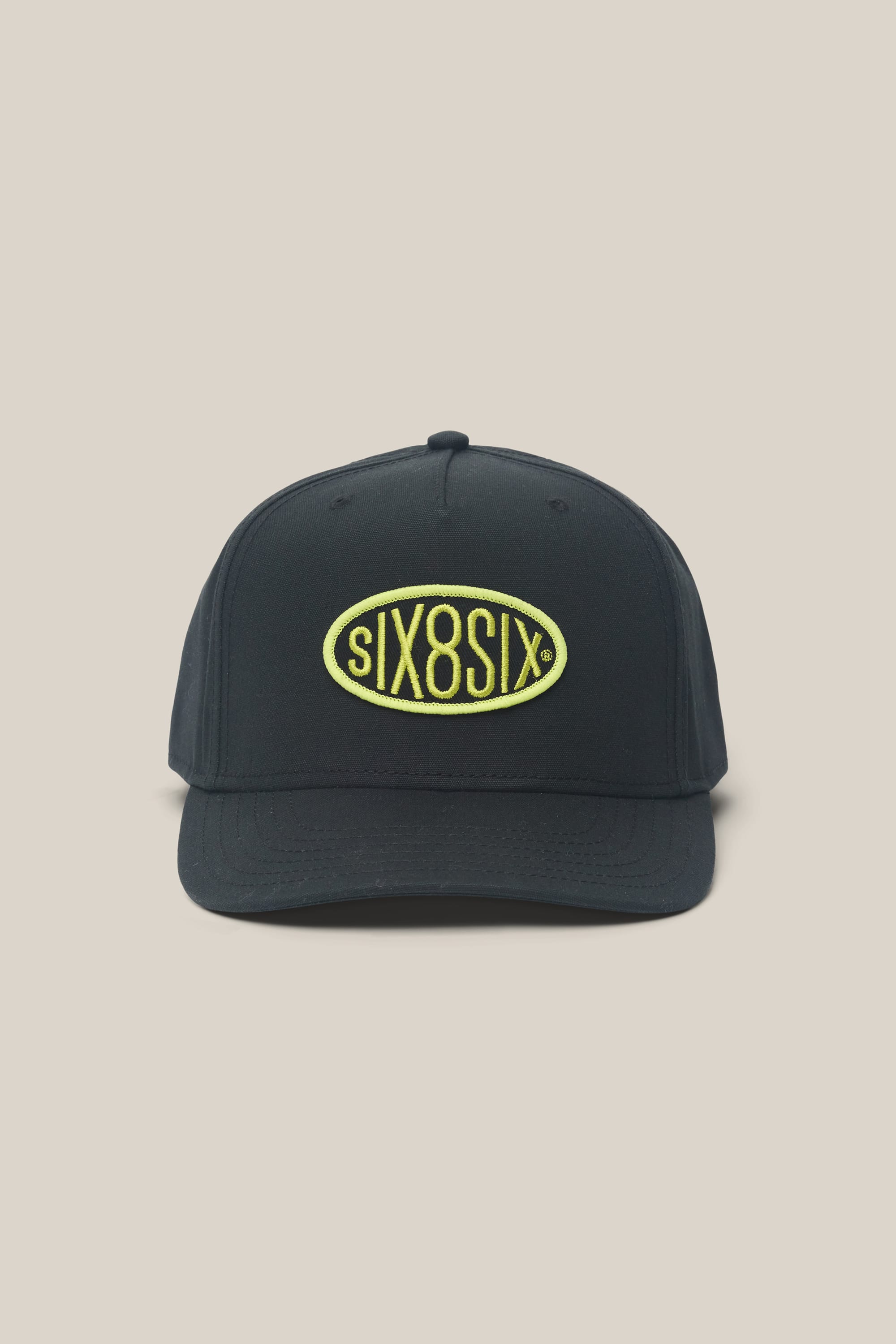 The 686 High-Pro 92 Structured 5 Panel Hat by 686 is a black men's poly-cotton hat with a curved brim, featuring a front yellow oval patch embroidered with black and white "sIX8SIX" text on a plain beige background.