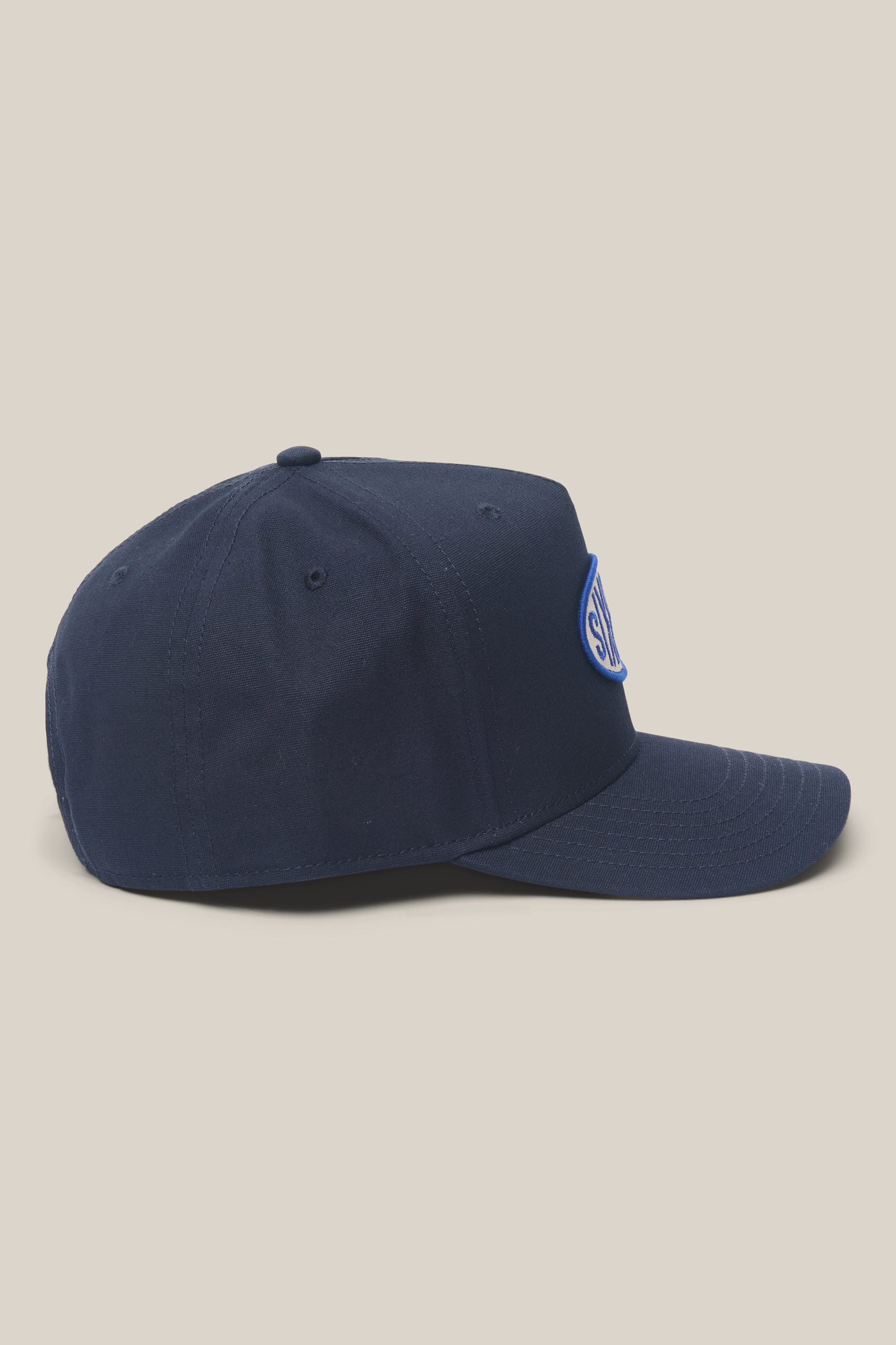 The 686 High-Pro 92 Structured 5 Panel Hat by 686 is a navy men's polyester cap with a curved brim, round button top, and blue-and-white patch on the front. Displayed side-on against a plain light beige background.
