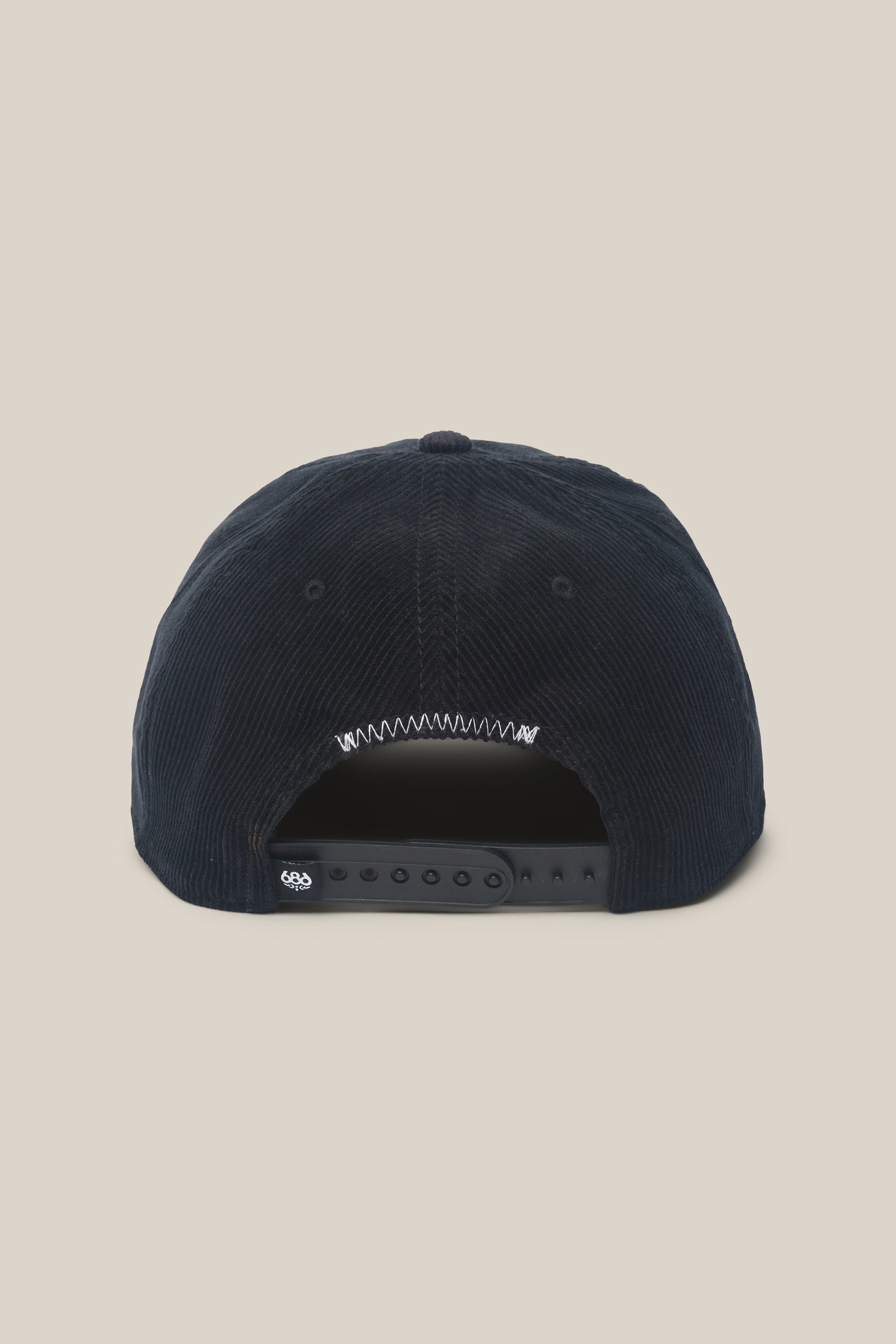 The 686 Mid-Pro Ghost Cord Unstructured 5 Panel Hat by 686 is displayed from the back, showcasing its adjustable snapback closure with multiple sizing holes. Crafted from a black polyester-cotton corduroy blend, this men’s hat delivers both style and comfort. The background is plain beige.