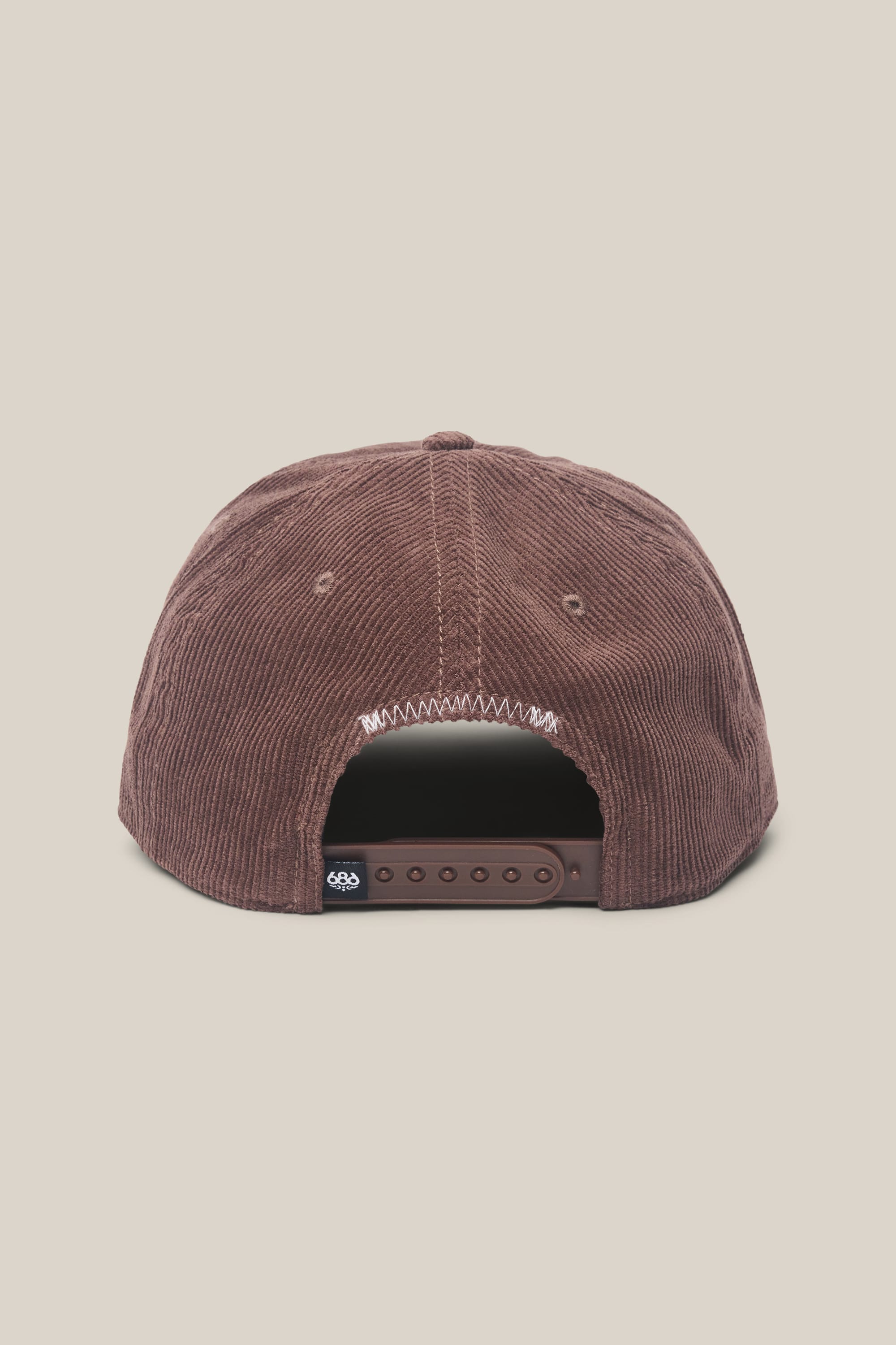The 686 Mid-Pro Ghost Cord Unstructured 5 Panel Hat by 686 is shown from the back, highlighting its brown corduroy design with a plastic adjustable strap and a small black tag on the left side of the strap. Crafted from durable polyester cotton woven fabric, this classic men's hat offers both comfort and style.