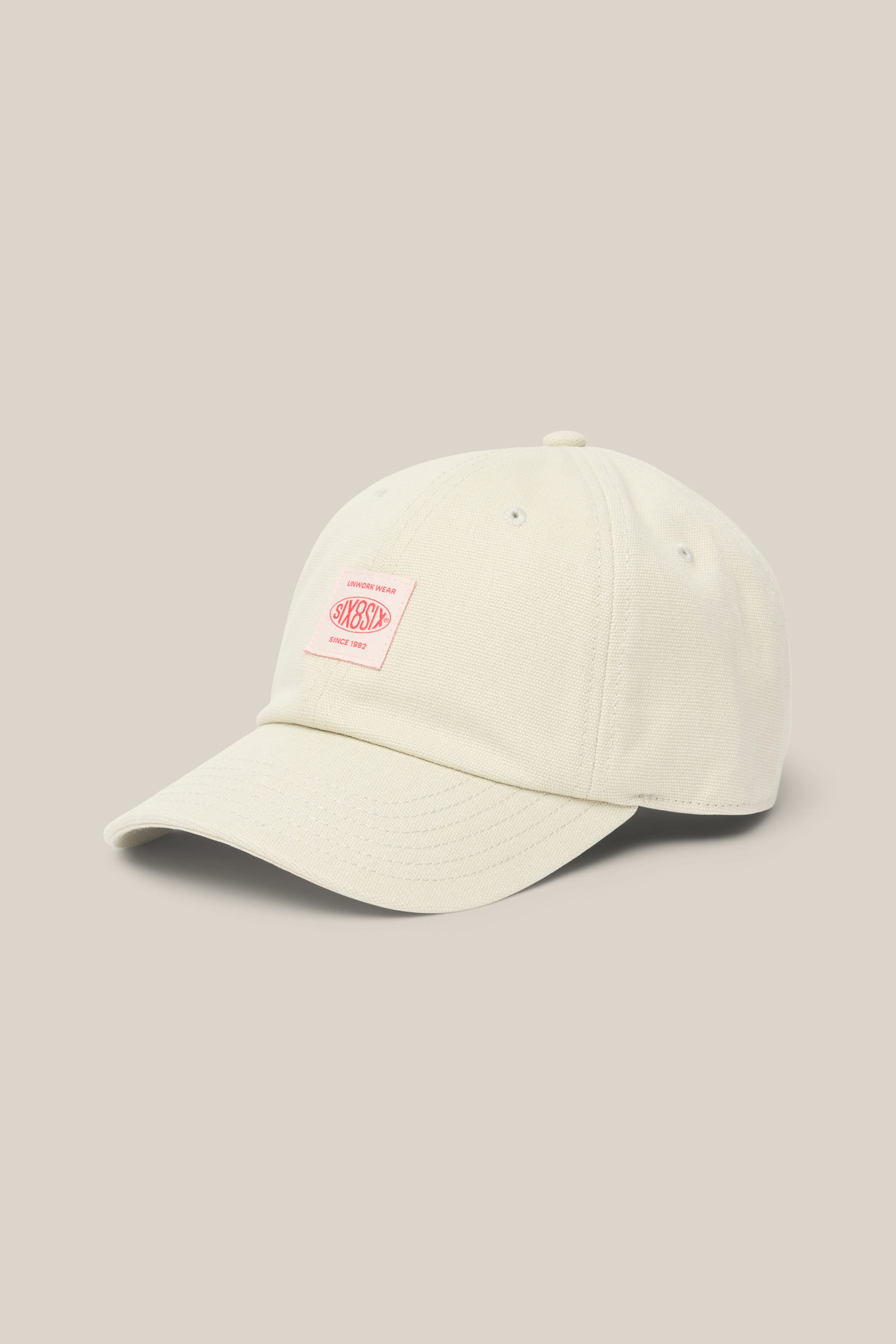 Here’s the rewritten sentence using the provided product data: The 686 Low-Pro Unwork Unstructured 6 Panel Hat by 686 features a cream-colored polyester-cotton blend, a curved brim, and a small rectangular pink and white patch on the front, displayed against a plain beige background. This stylish men’s hat combines comfort with understated design.