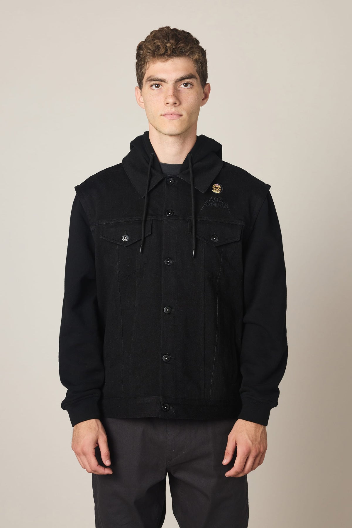 A person wearing a 686 Men’s Metalhead Trucker Jacket, a black denim men’s woven jacket featuring a hooded sweatshirt integrated into the collar.