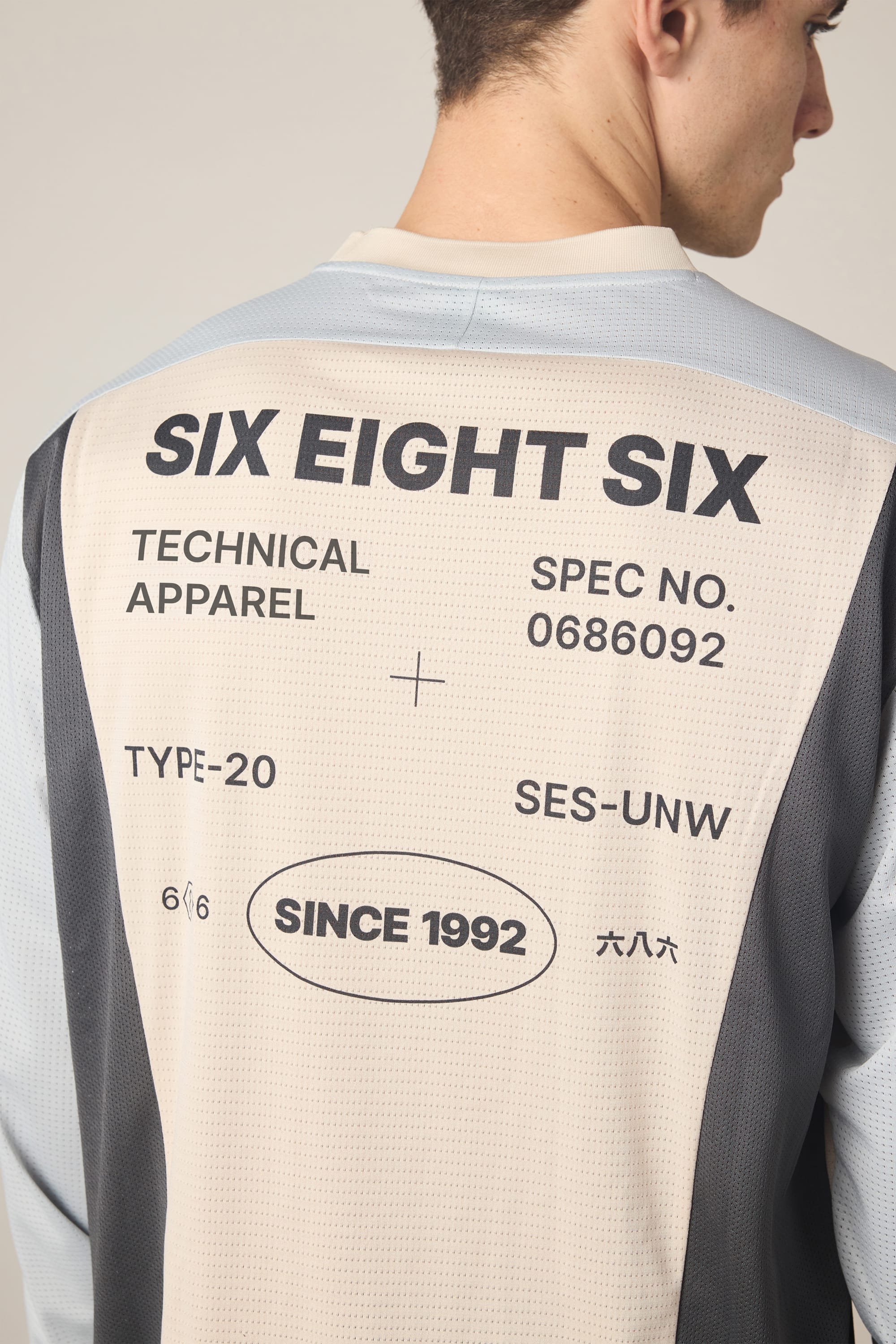 A person shown from the back wears the 686 Men's Hex Turbo LS Tech Tee, a men's polyester shirt in light and dark gray by 686, featuring large black text reading SIX EIGHT SIX, TECHNICAL APPAREL, SINCE 1992, plus other numbers and symbols.