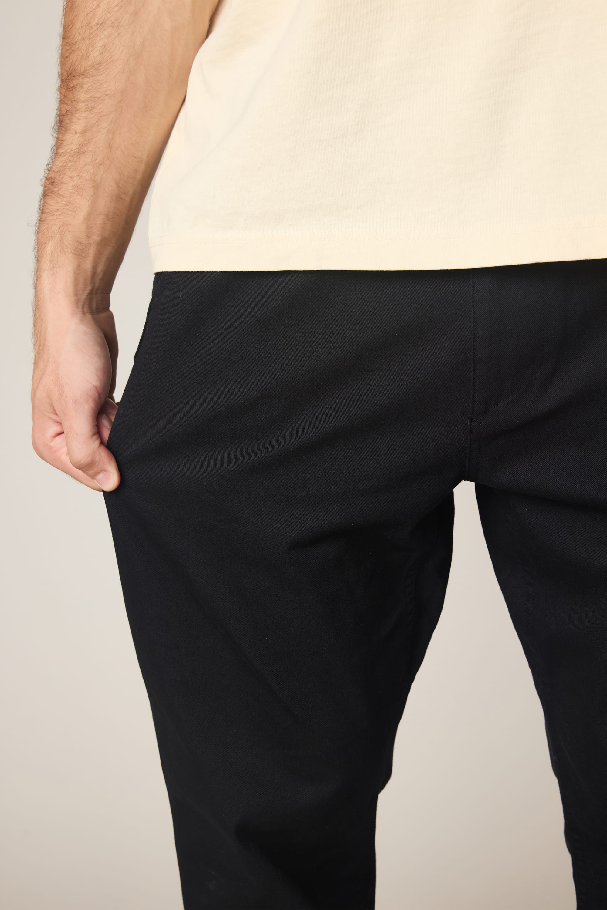 A person wearing a cream-colored shirt and black 686 Men's Unwork® Tradesman Pant - Relaxed Fit, shown from the waist down, gently grips the fabric near their hip with their left hand.