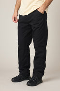A person stands with hands in pockets, wearing 686 Men's Unwork® Tradesman Pant - Relaxed Fit by 686, a light shirt, and black sneakers, photographed from the shoulders down against a plain background.