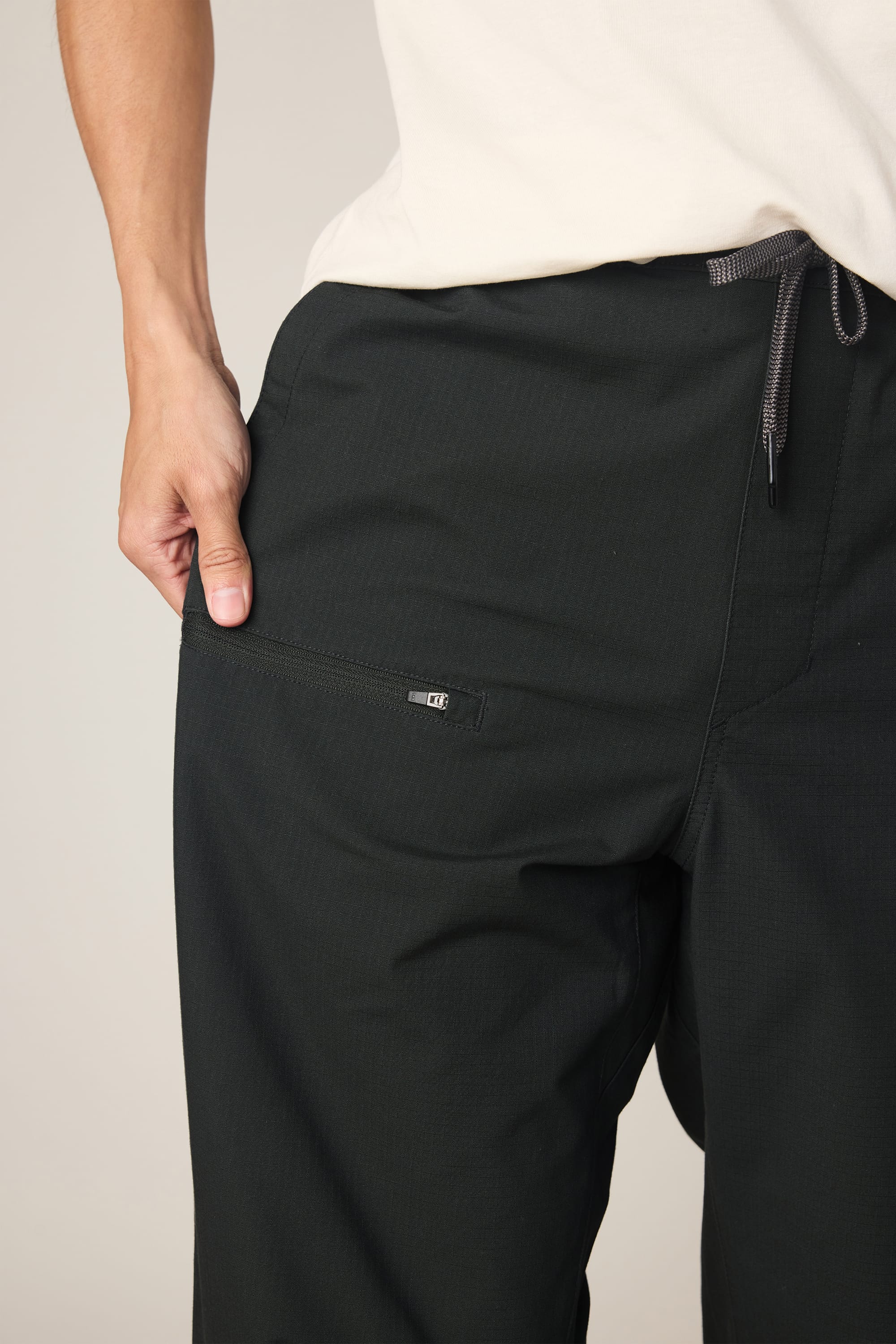 A person in the 686 Men's Free Loader Pant - Loose Fit by 686 stands with a hand in their pocket, highlighting the stylish nylon woven fabric, zippered pocket, and drawstring waist.