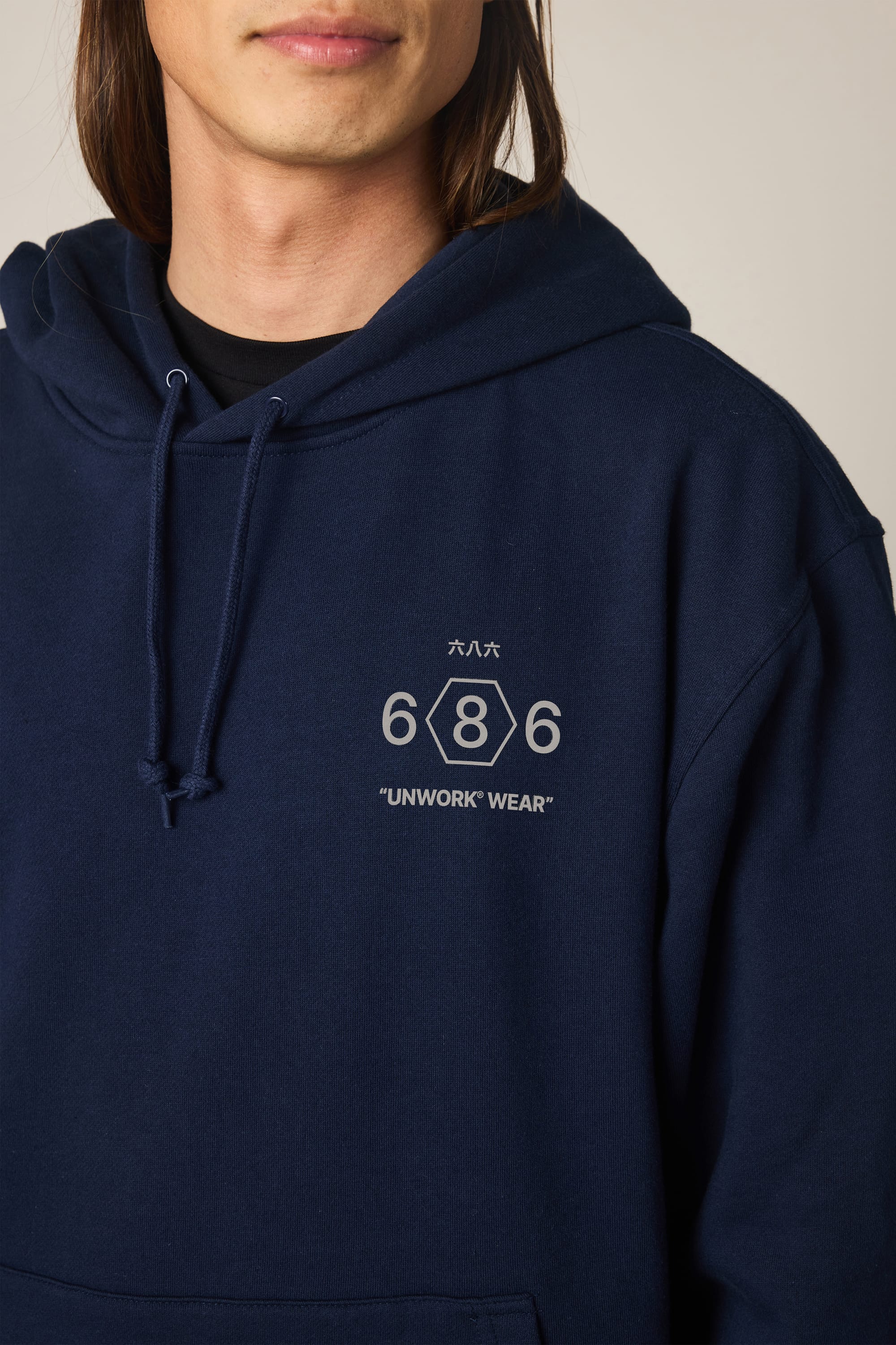 A person wears the 686 Men's Unwork Spec Athletic LS Hoody, featuring "686 UNWORK WEAR" and Japanese text on the chest. Only the lower face and upper torso are visible.