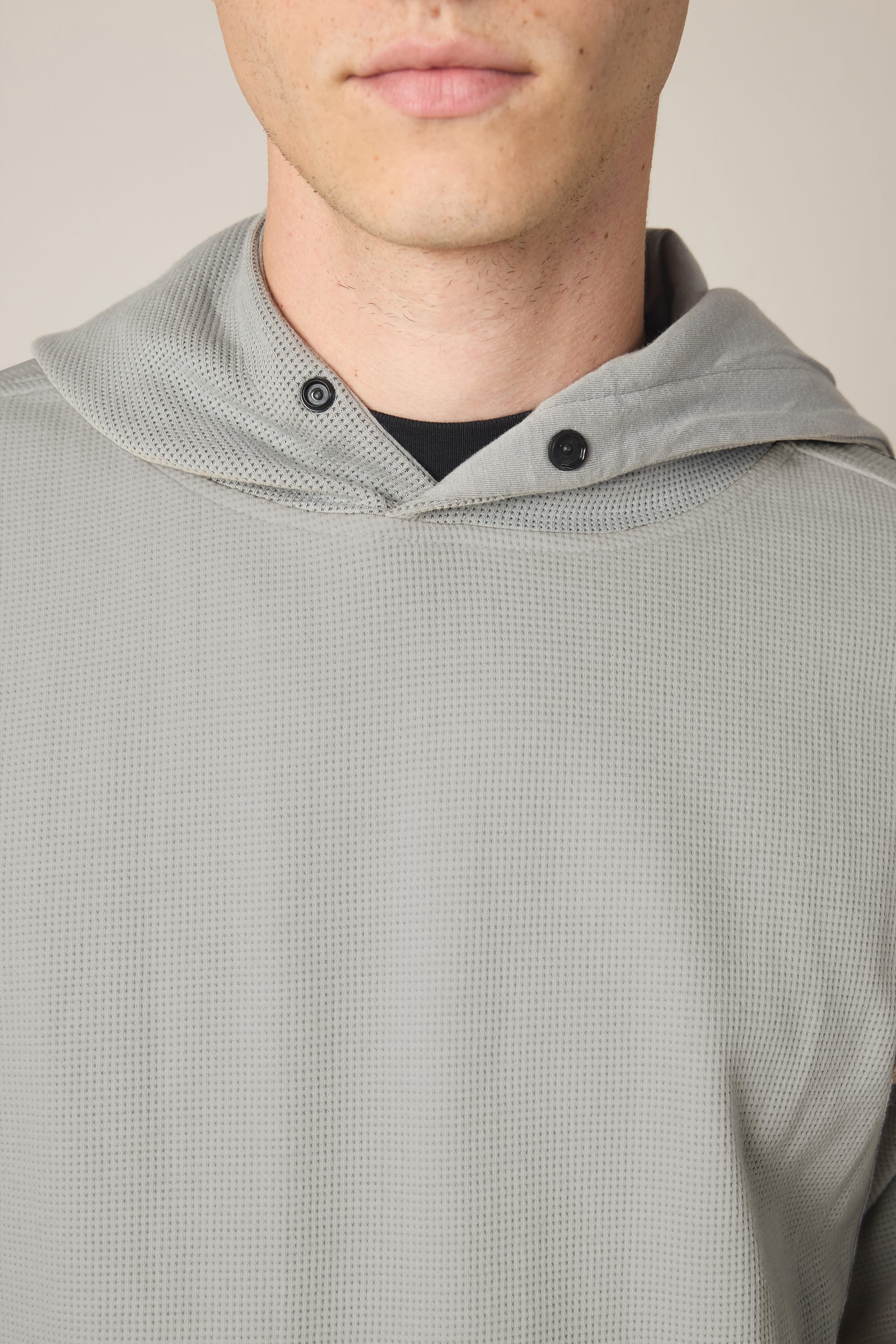 A close-up of a person wearing the 686 Men's Let's Chill Waffle Hoody in light gray, featuring black buttons at the neckline and layered over a men's t-shirt, with only the lower face and upper torso visible.