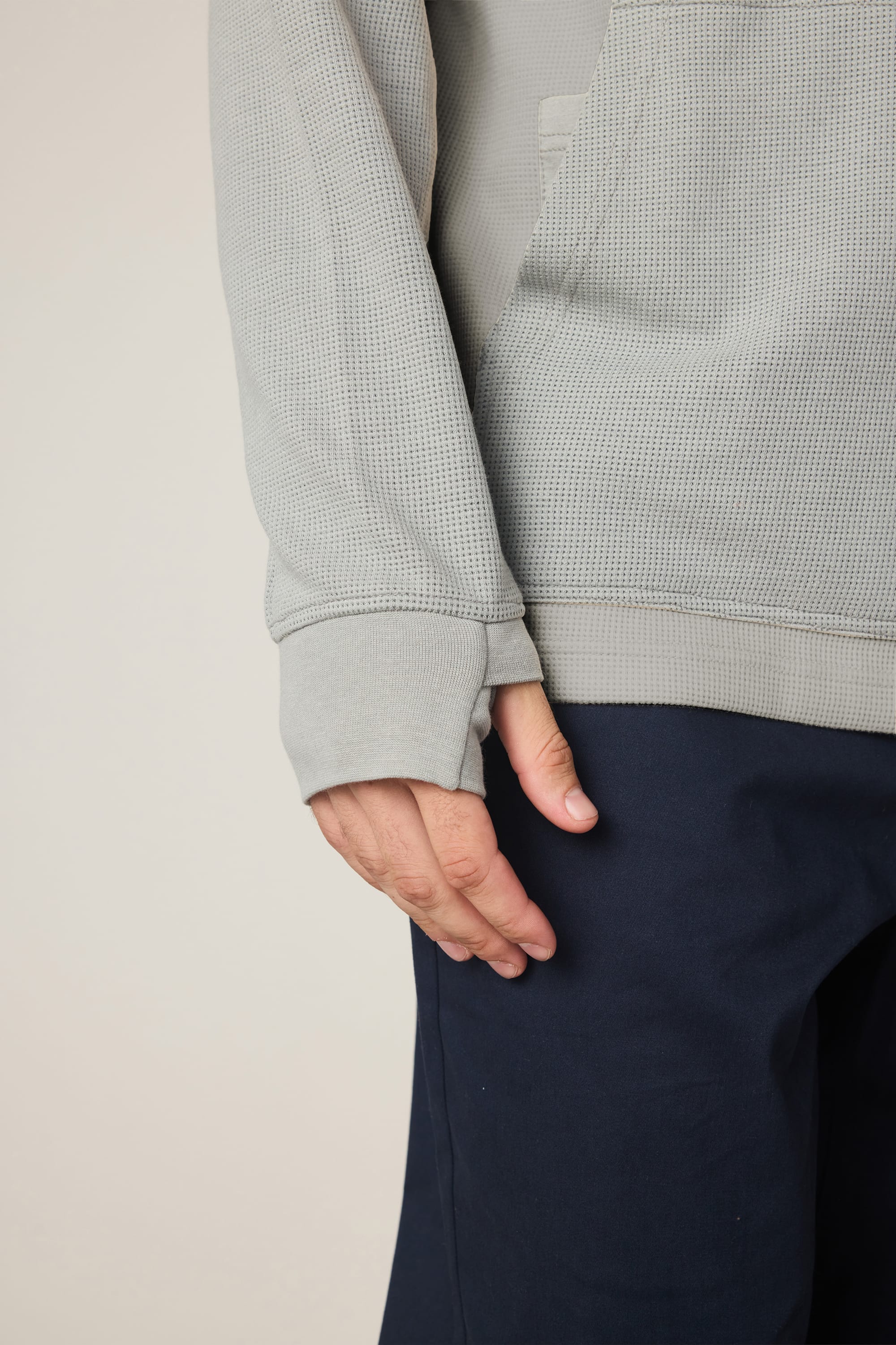 A person wearing the 686 Men's Let's Chill Waffle Hoody in light gray with dark pants rests their left hand by their side. The focus is on the hoody's sleeve, hand, and hip area against a neutral background.
