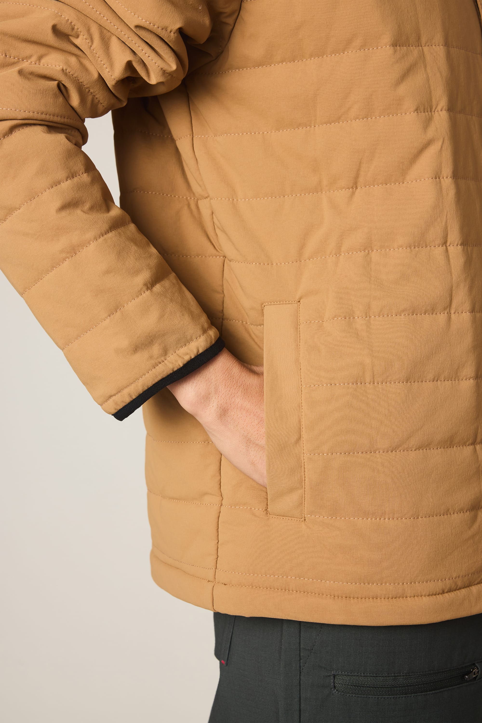 A person wears the 686 Men's Thermaldry Insulated Shacket in tan, one hand casually in the side pocket, shown from chest down against a plain background.