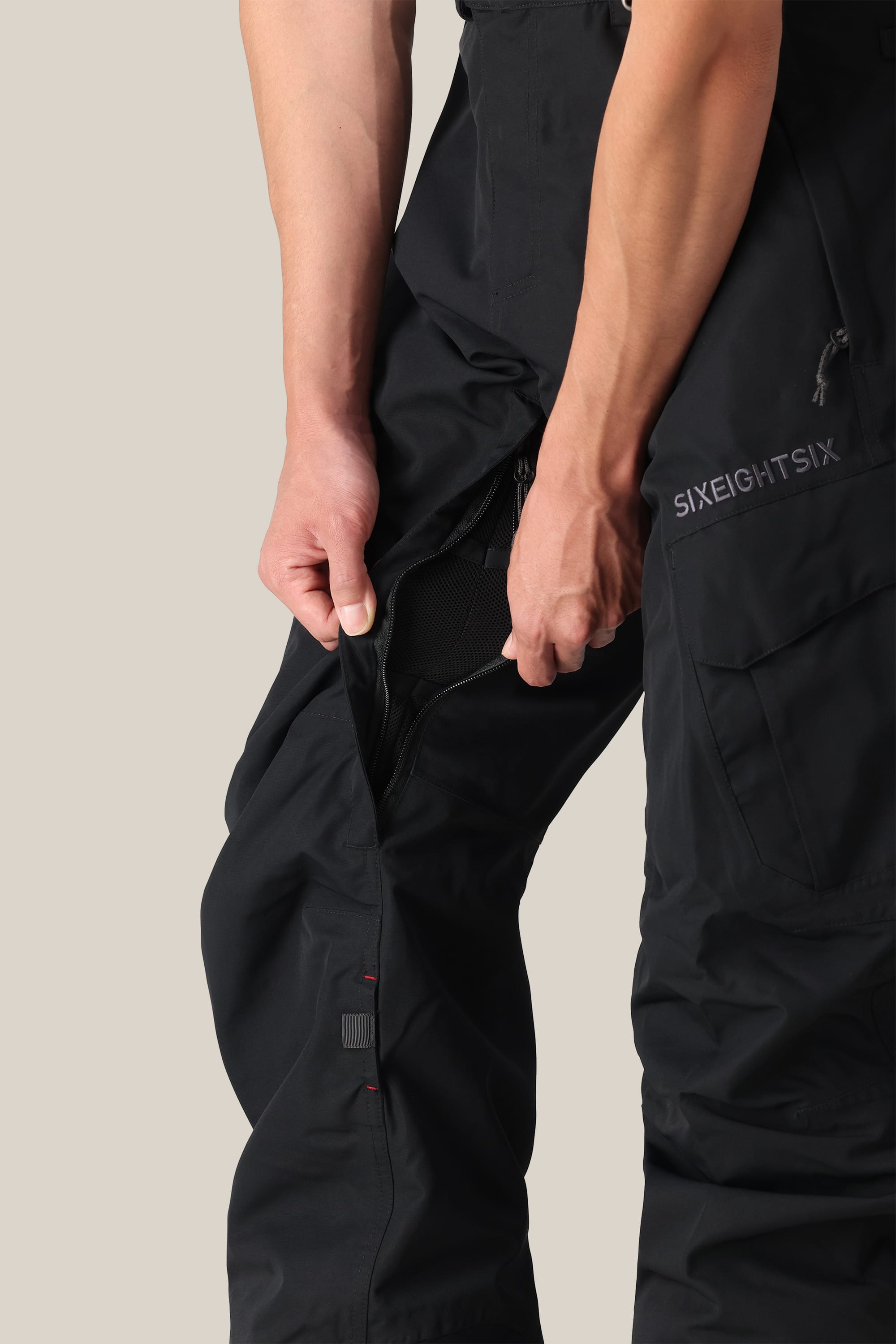 A person unzips a ventilation opening on the side of black 686 Men’s SMARTY® 3-in-1 Cargo Pant, revealing a mesh lining inside.