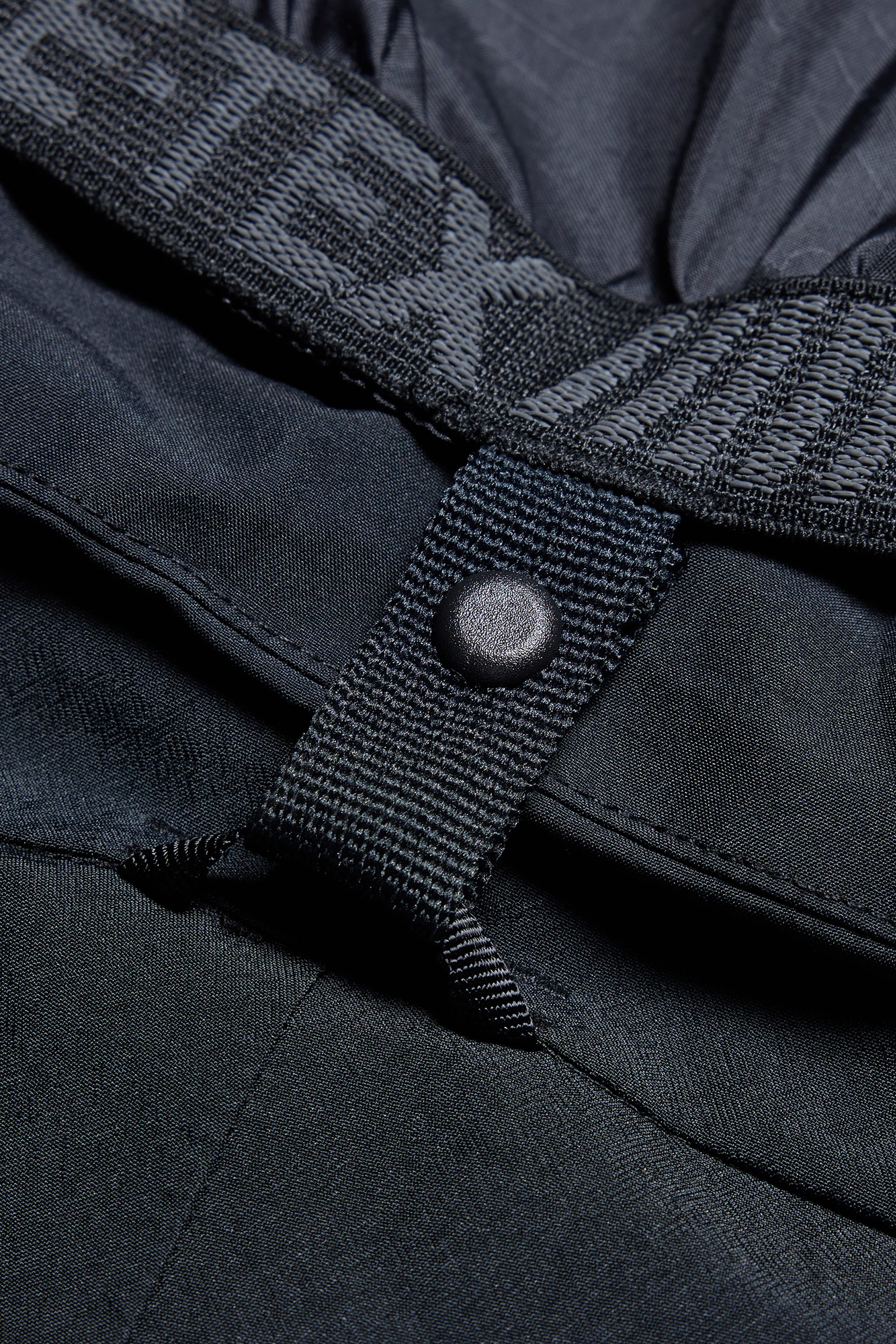 Close-up view of a black snap button attached to a fabric loop on the 686 Men’s SMARTY® 3-in-1 Cargo Pant, with part of the elastic waistband featuring faint branding visible at the top.
