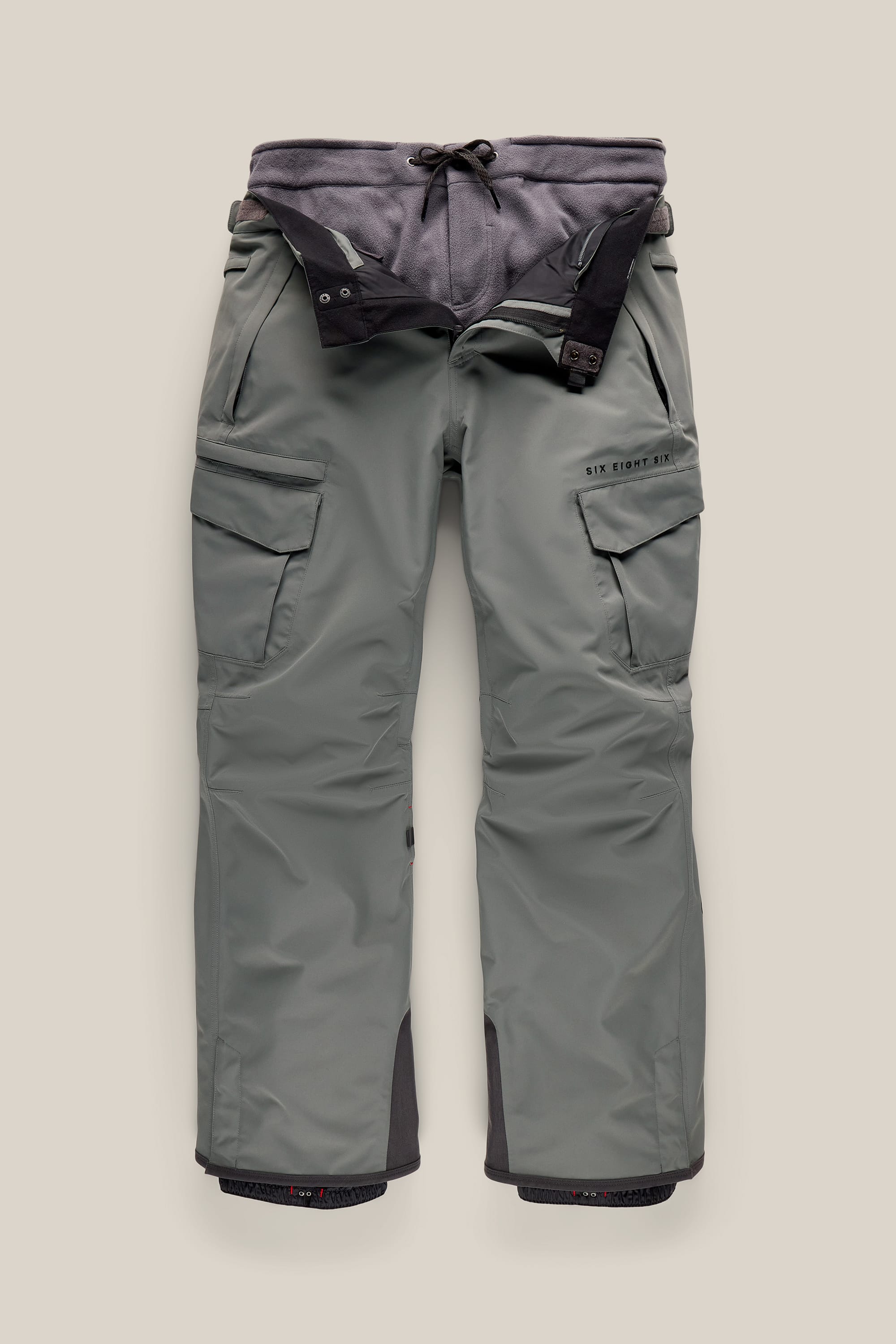 The 686 Men’s SMARTY® 3-in-1 Cargo Pant by 686, shown in gray with black adjustable suspenders, features multiple cargo pockets, reinforced cuffs, and visible seams, displayed flat on a neutral background.