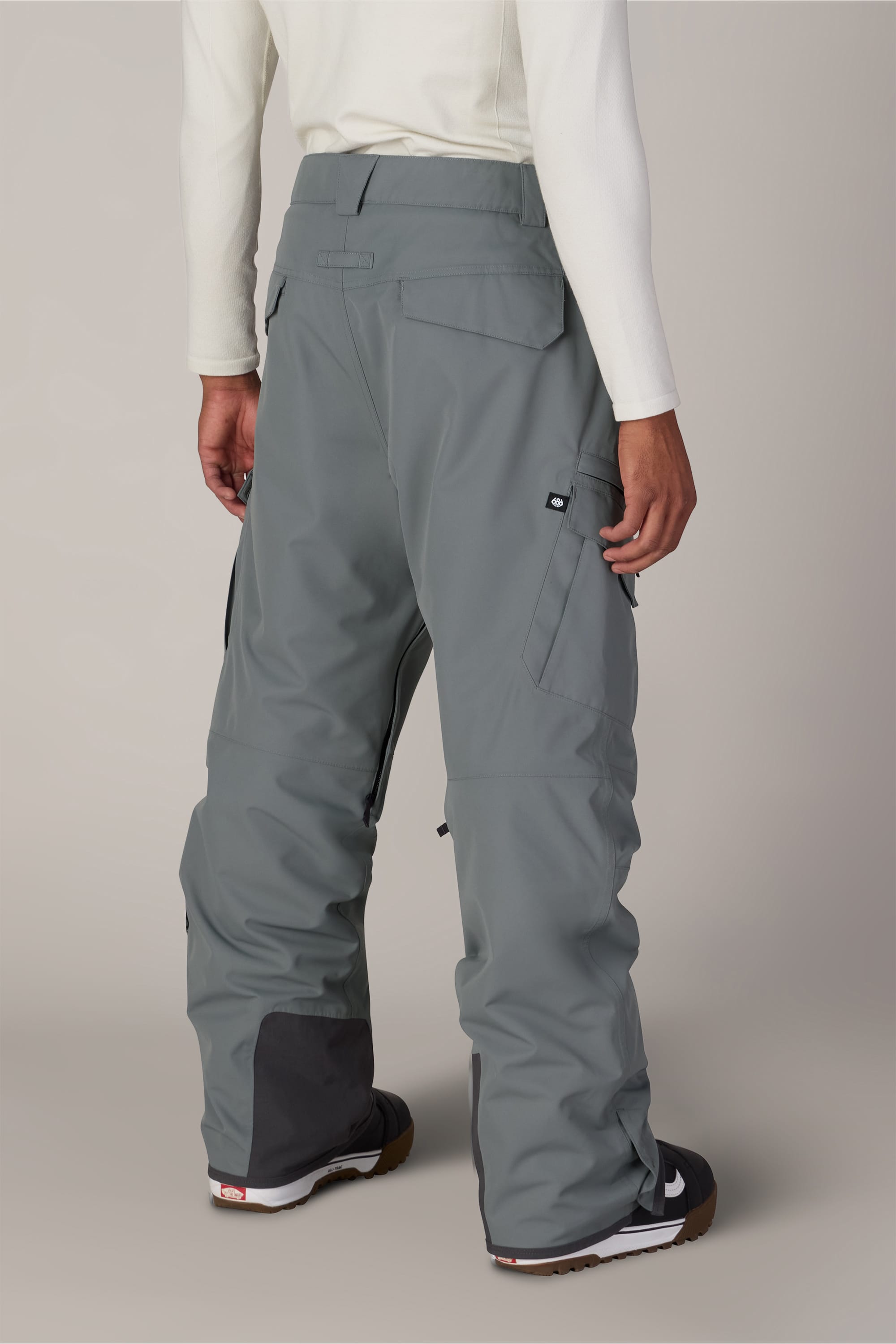 A person is wearing 686 Men’s SMARTY® 3-in-1 Cargo Pant in gray, paired with a white long-sleeve shirt and black-and-white sneakers, standing with their back to the camera against a plain light background.