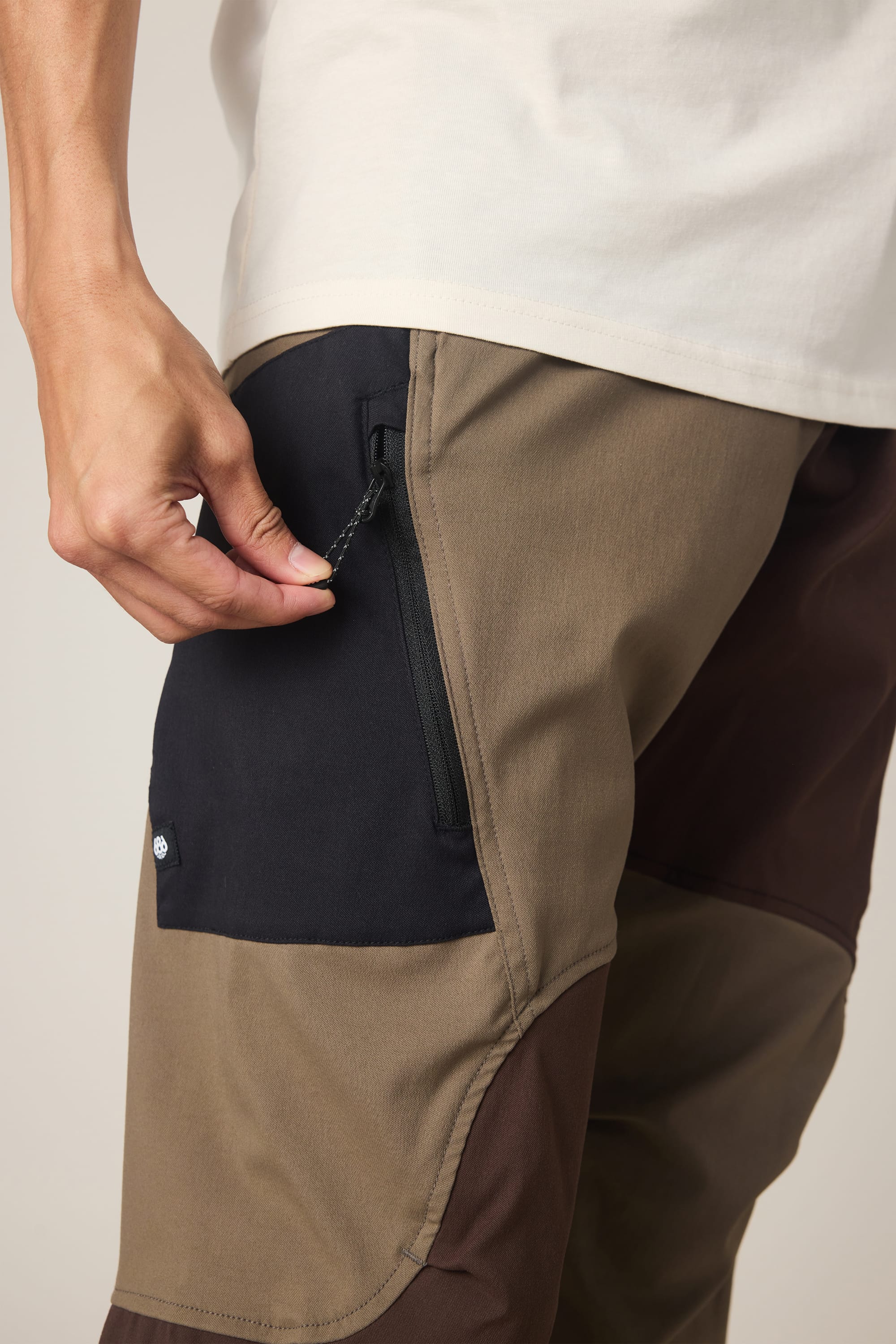 A person wearing the 686 Men's Anything Cargo Pant - Relaxed Fit unzips a black pocket on the left thigh. Only their lower torso and hand are visible.