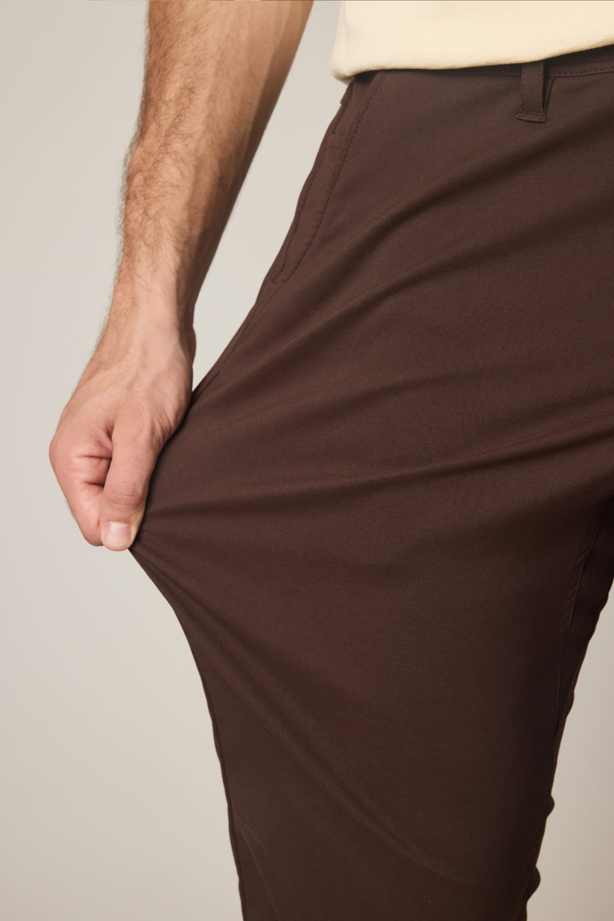 Wearing the 686 Men's Everywhere® Pant - Relaxed Fit, a person stretches the fabric outward with one hand to demonstrate its flexibility.