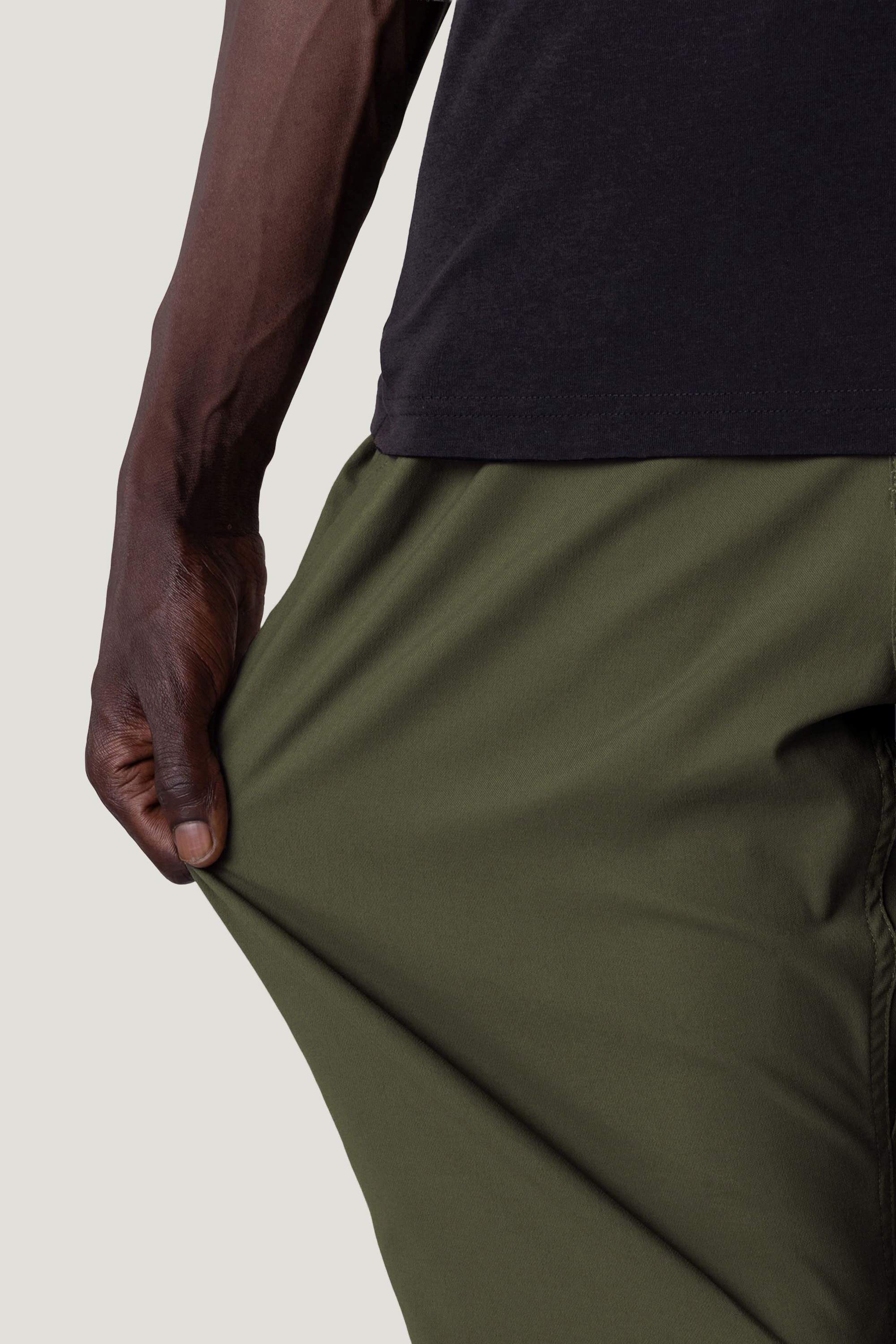 A person wearing the 686 Men's Everywhere® Pant - Relaxed Fit in olive green stretches the fabric to demonstrate its flexibility.