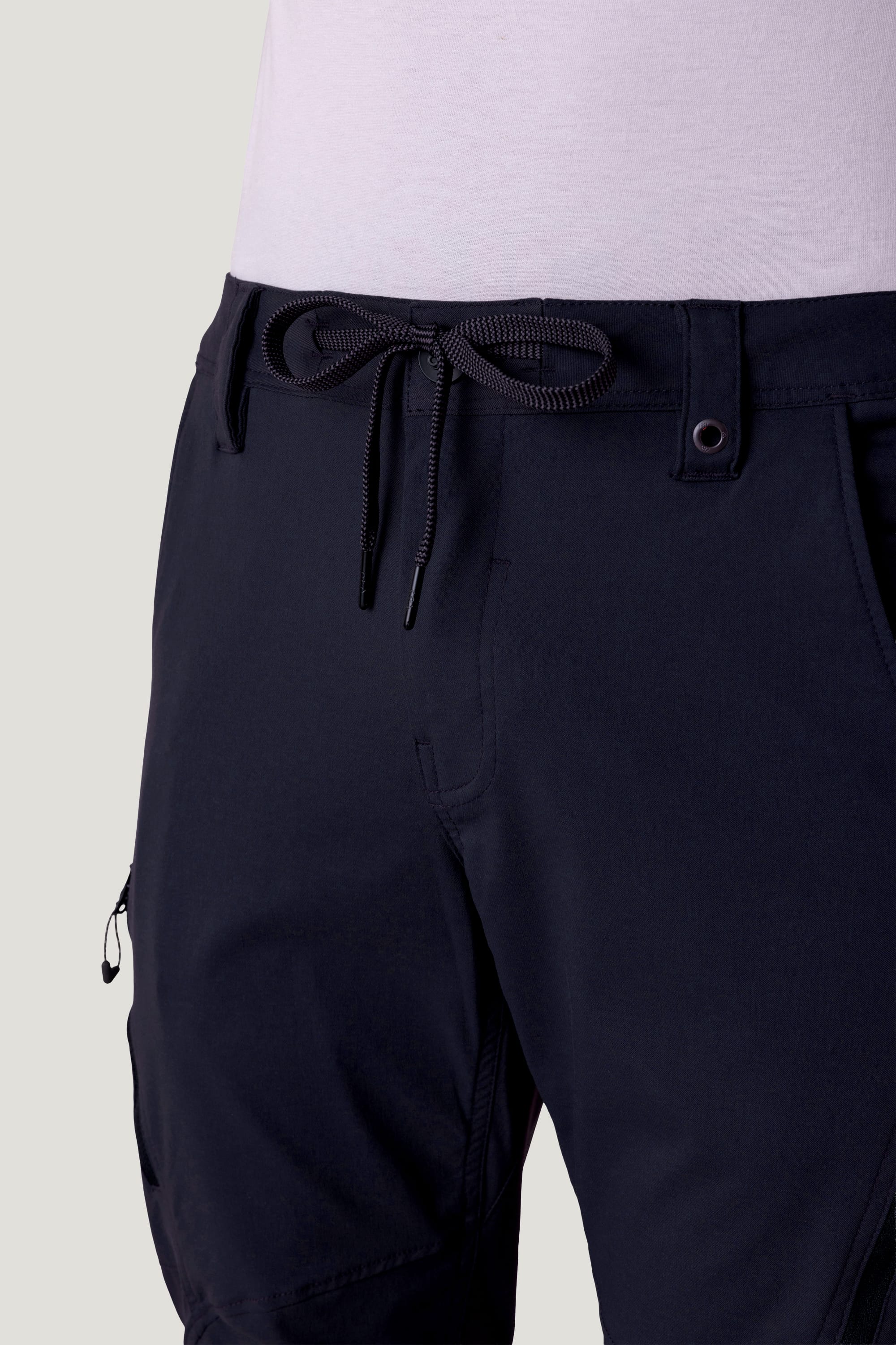 Close-up of a person wearing 686 Men's Anything Cargo Pant - Slim Fit by 686, featuring a drawstring waist and adventure-ready 13-pocket details at the waist and sides with a light-colored shirt tucked in.