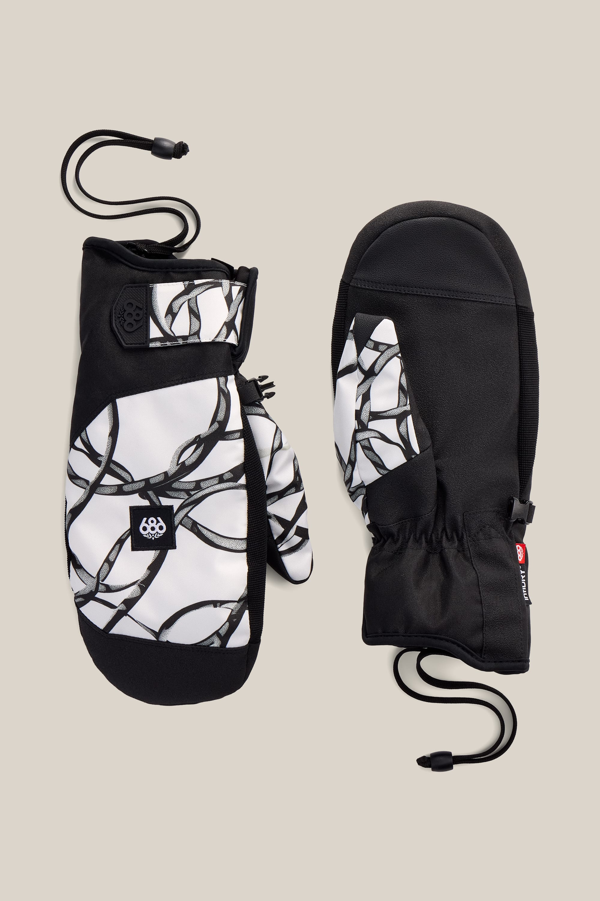 Two 686 Men’s Primer Mitts with black palms and a black-and-white chain pattern on the tops, featuring adjustable wrist straps and attached cords, are displayed on a neutral beige background.