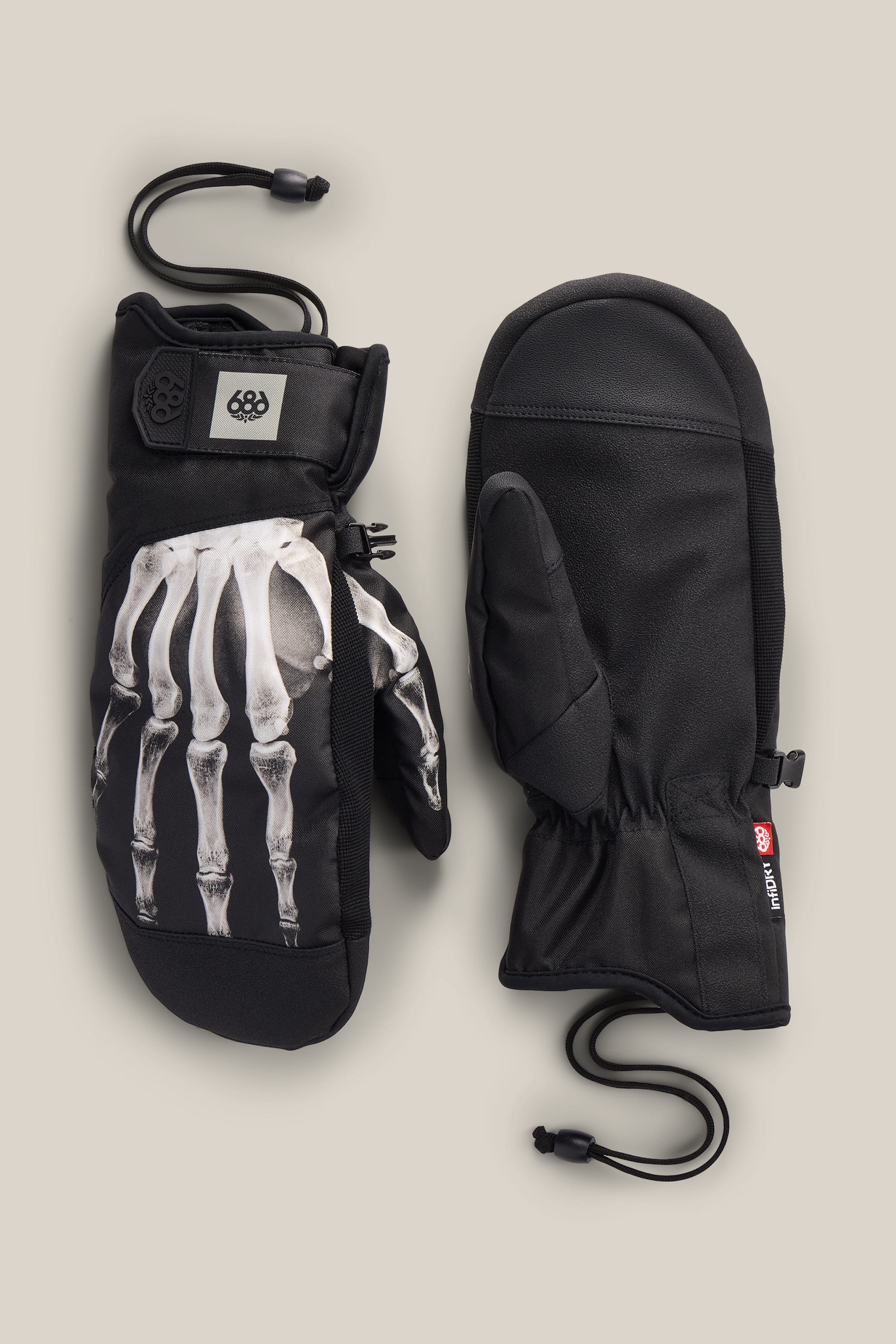 A pair of 686 Men’s Primer Mitts in black, one displaying a white skeleton hand print on the back. Both mittens by 686 feature elastic wrist cords and are shown on a plain, light background.