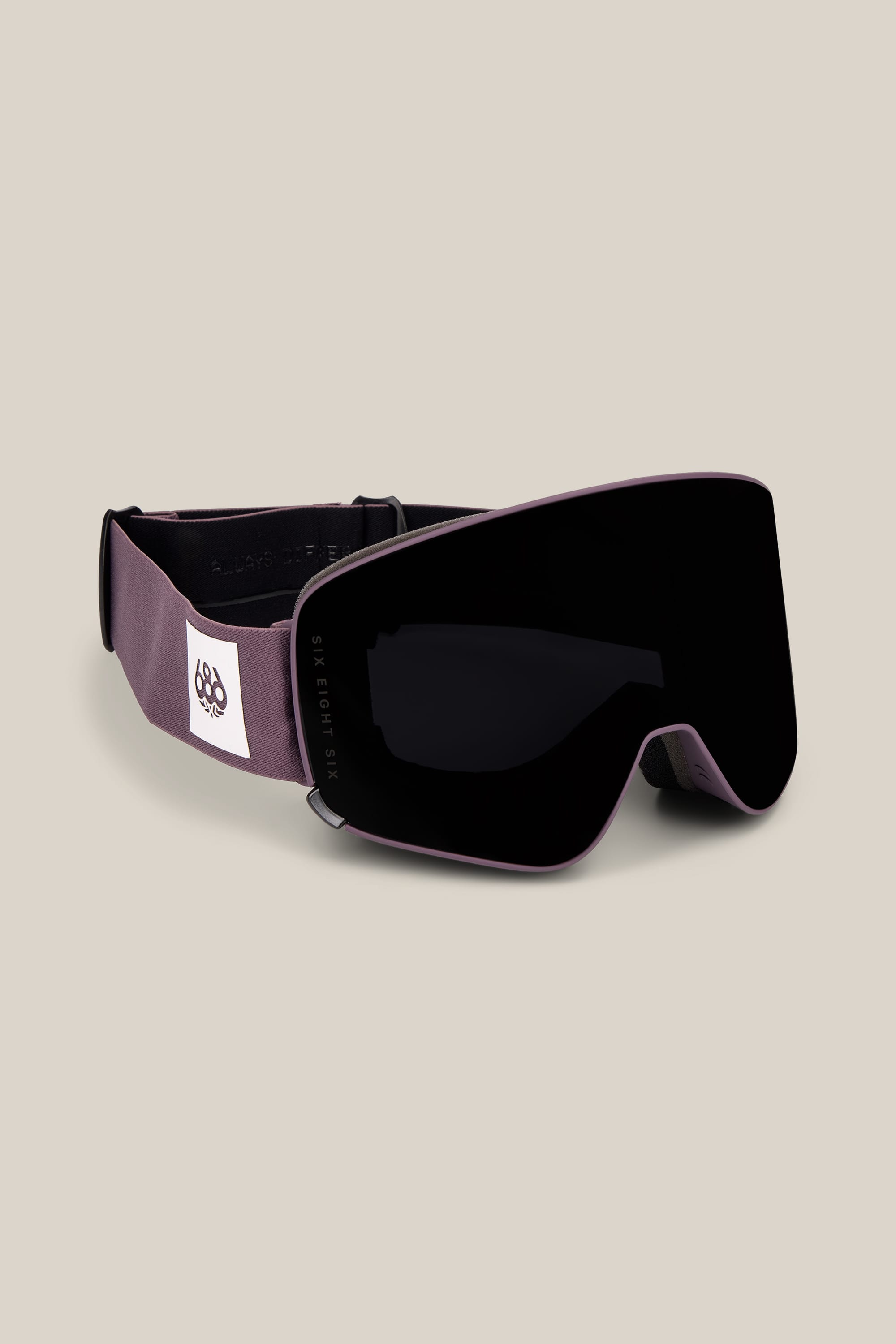 The 686 SMARTY® Magnetic Goggle by 686, shown in matte black with a wide, curved lens and a dark gray strap featuring a white patch with a geometric logo, is displayed against a light beige background.