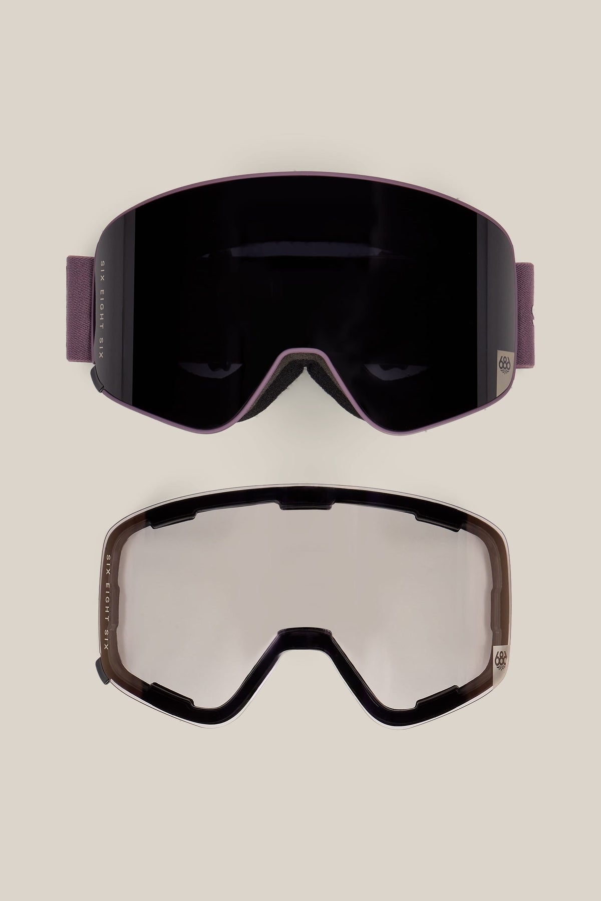 Two pairs of 686 SMARTY® Magnetic Goggles by 686 are displayed on a beige background: one features a dark, reflective lens while the other has a clear lens. Both goggles share the same sleek shape and design.