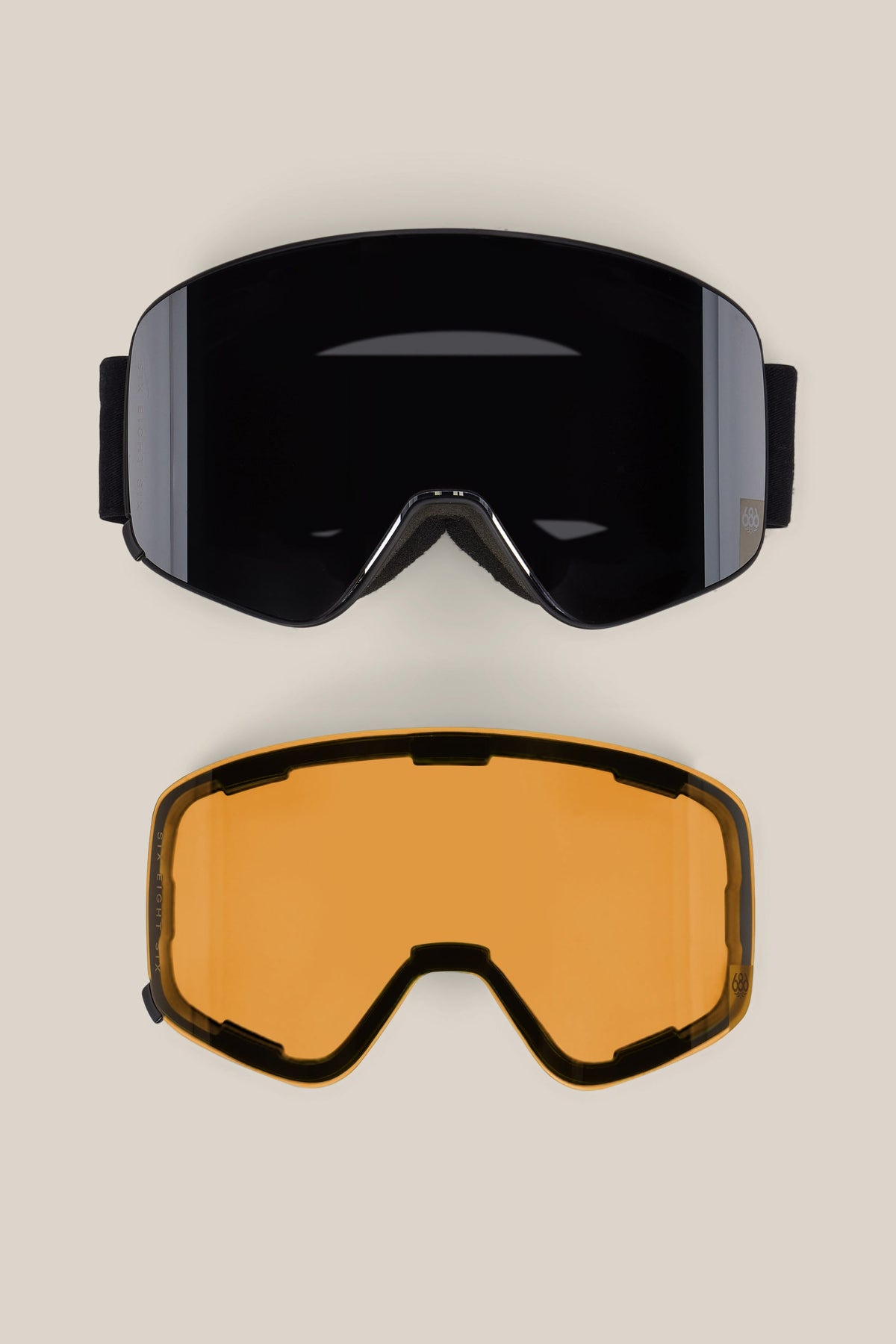 The 686 SMARTY® Magnetic Goggle by 686 is shown with two interchangeable lenses—one dark and reflective, the other amber-tinted. Both curved lenses are displayed on a plain beige background.