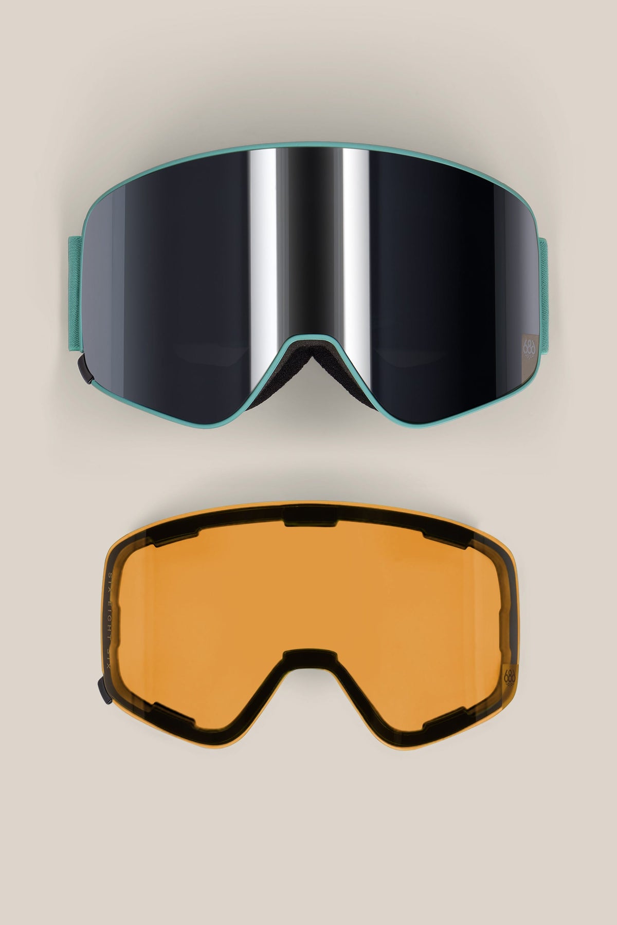 The 686 SMARTY® Magnetic Goggle by 686 is shown with two interchangeable lenses: a reflective black lens attached to the goggles on top, and a separate amber lens below, both displayed on a beige background.